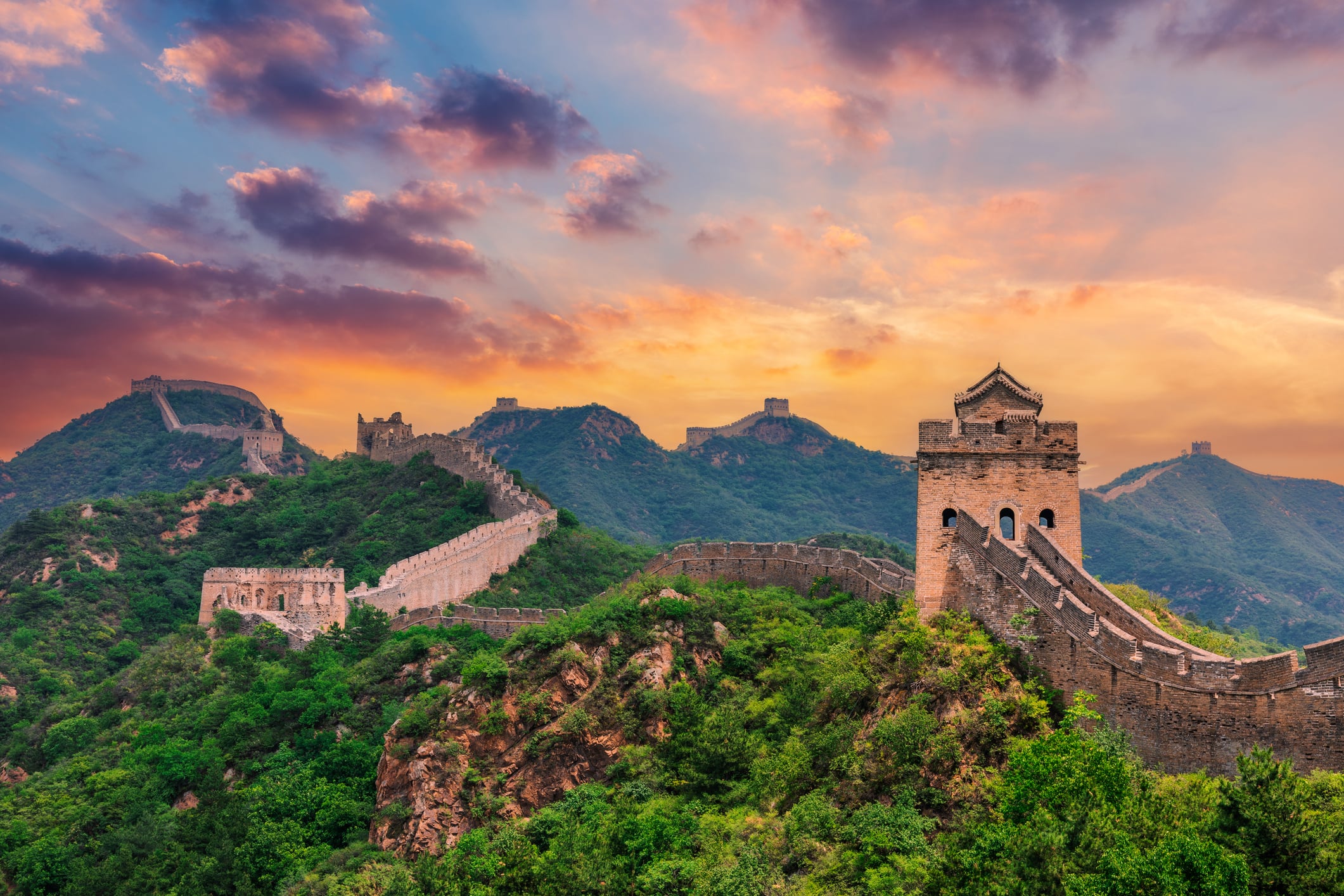 The Great Wall of China stretching across lush green mountains at sunset.