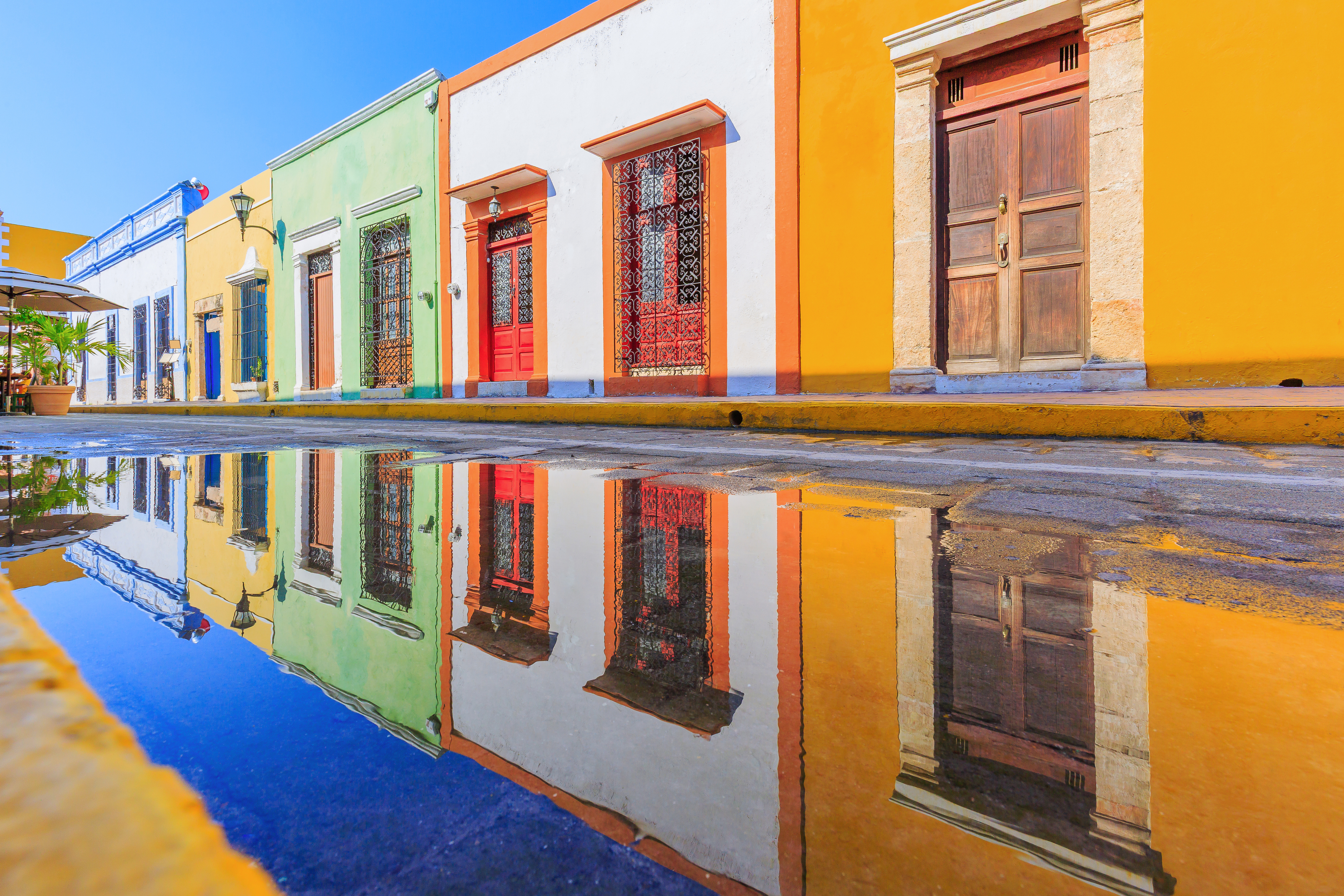 A line of bright, colourful cubic buildings in Campeche's old town, Mexico, reflected clearly in a puddle in the street