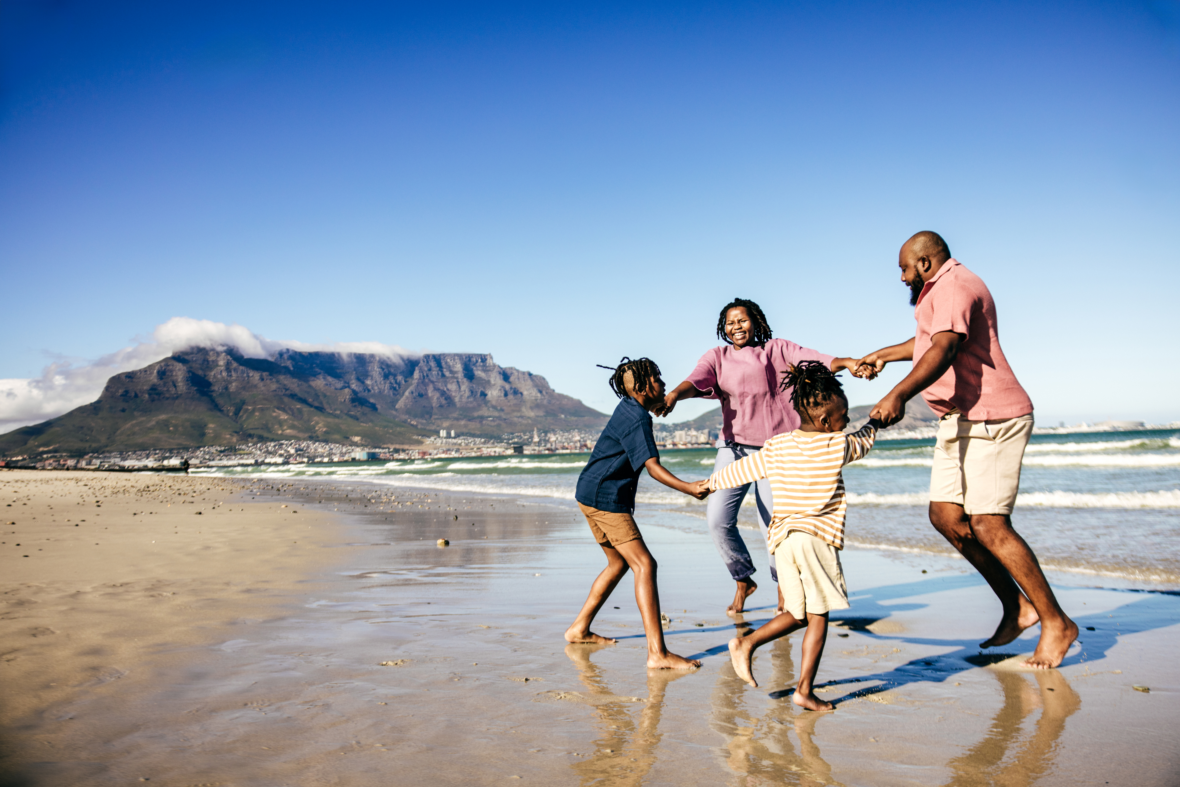 A happy family plays together on the beach in front of Table Mountain in Capteown, South Africa, their laughter echoing over the waves.