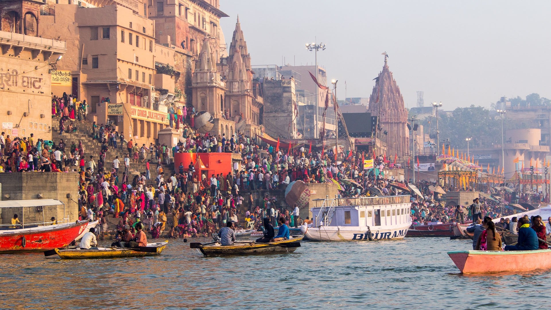 people on boats and ghats alongside the river celebrating a festival