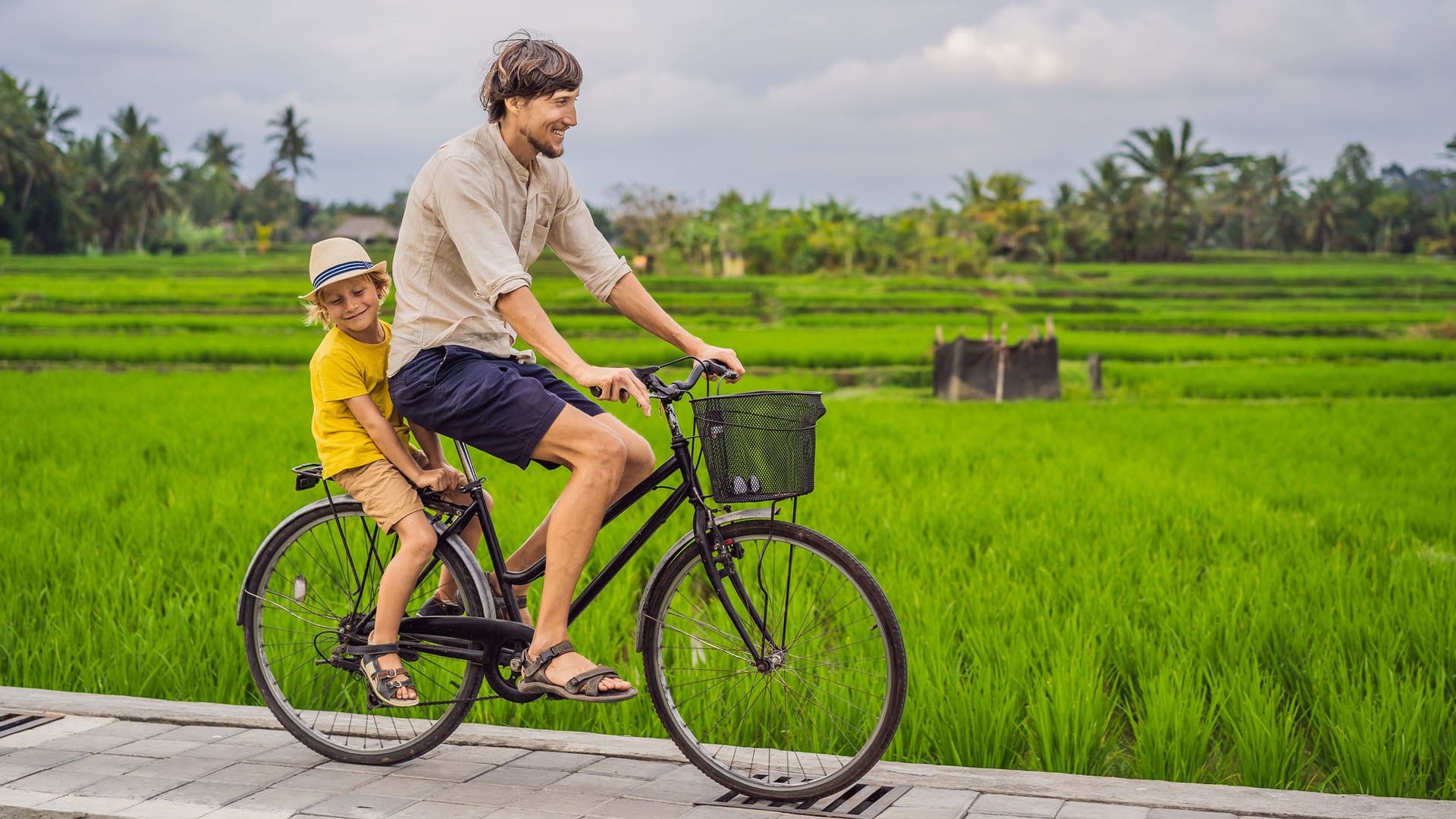 A father cycling through rice paddies with his son.