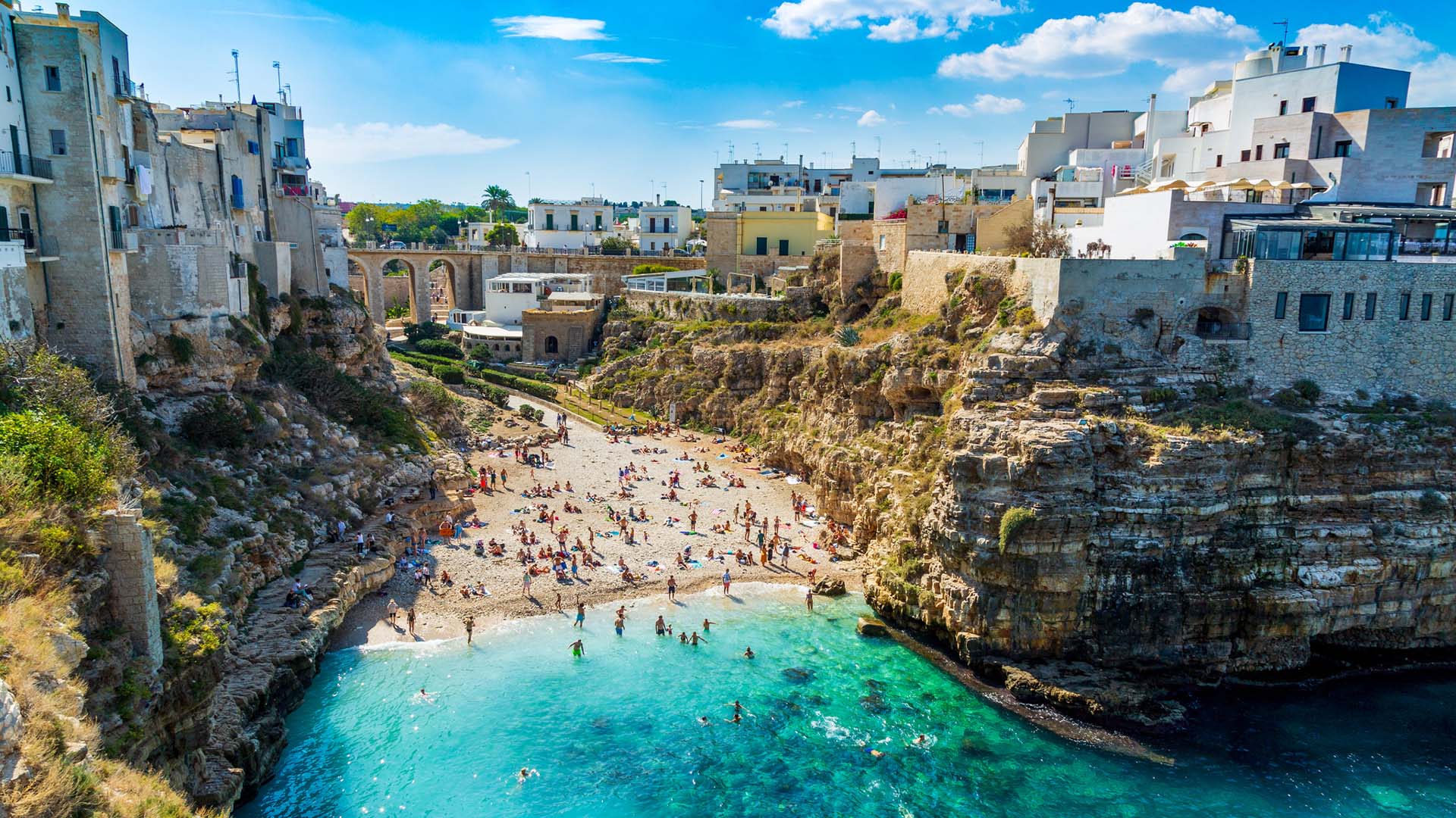 A beach with swimmers surrounded by home son cliffs in Polignano a Mare in Italy.