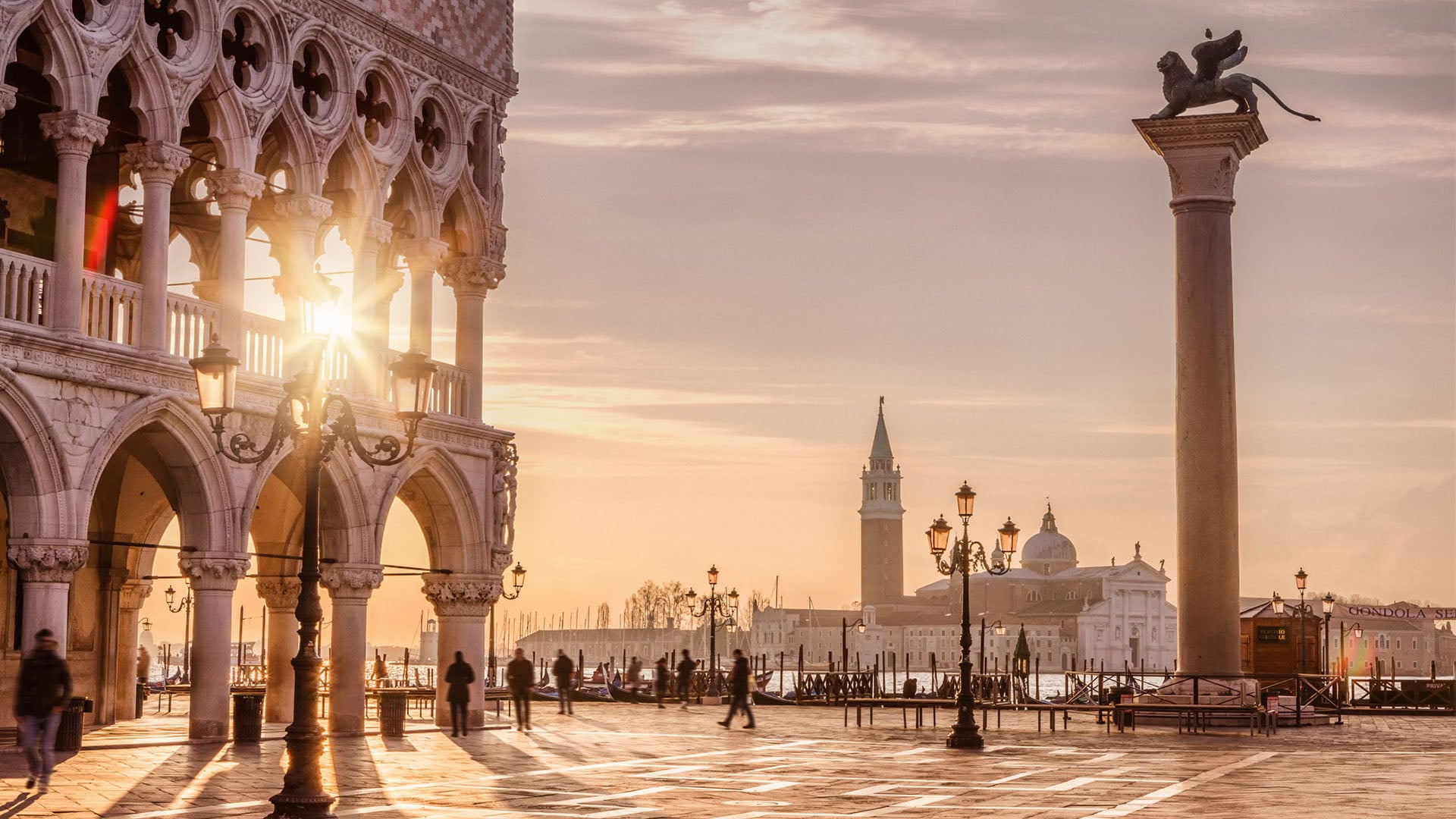 People walking through St. Mark's Square in Venice at sunrise.