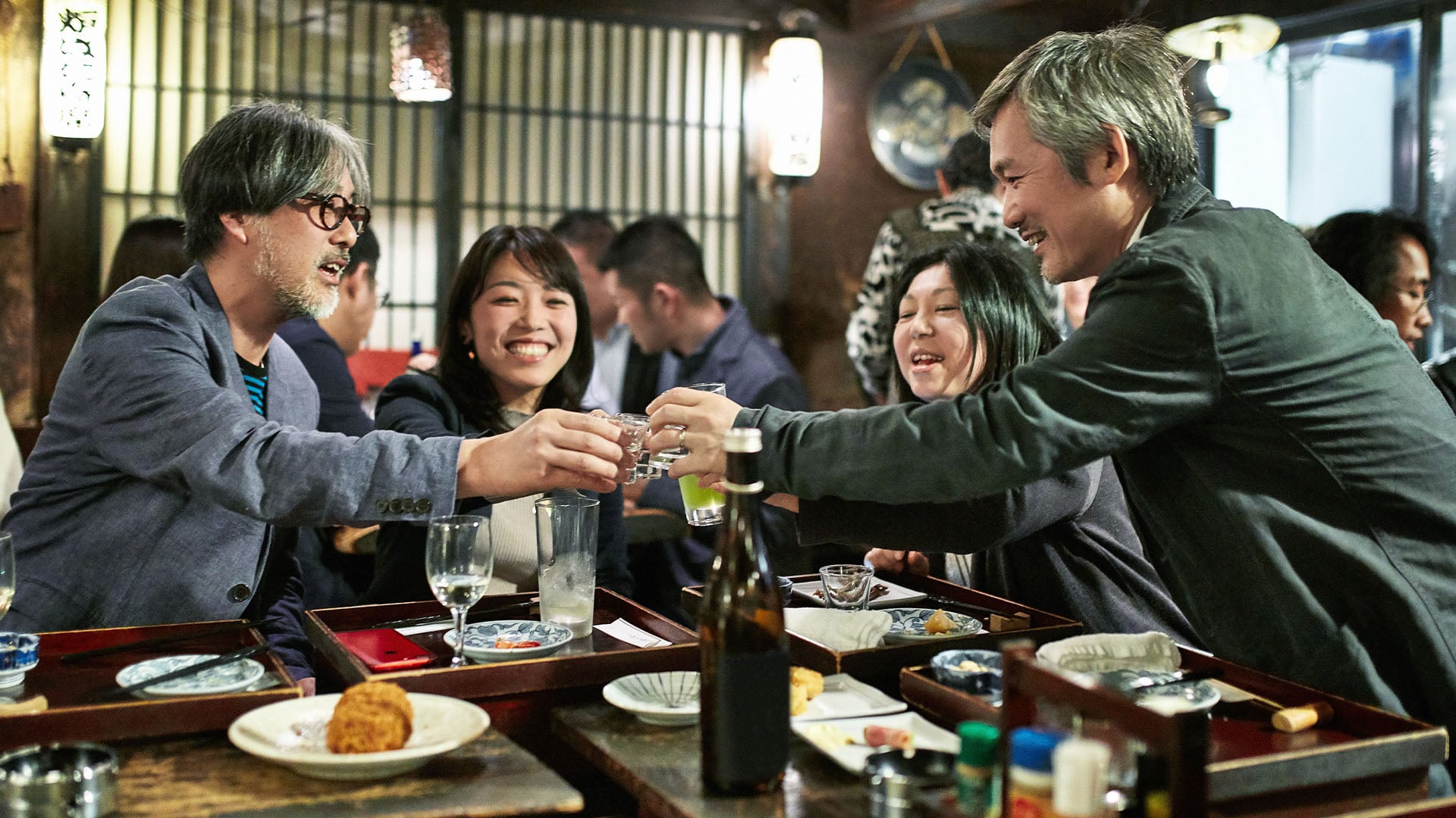 A group of Japanese people celebrate with cheers at a bar.