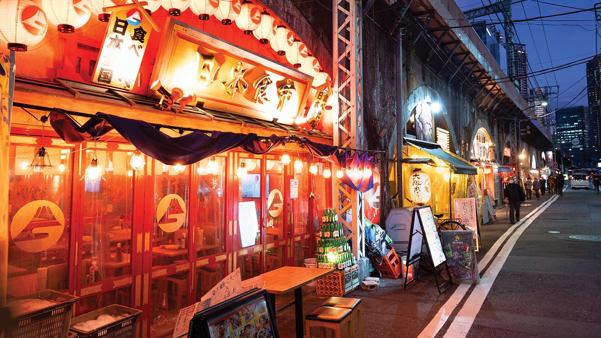 A brightly lit restaurant along a city street in Tokyo at night