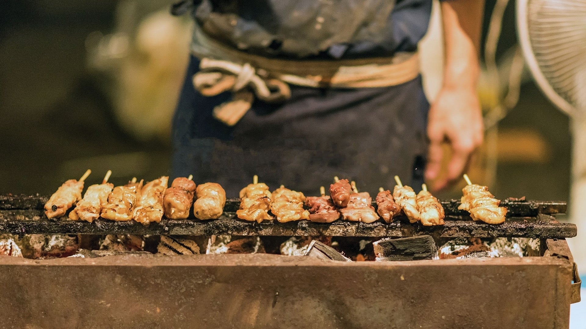 A chef grilling yakitori on a charcoal grill
