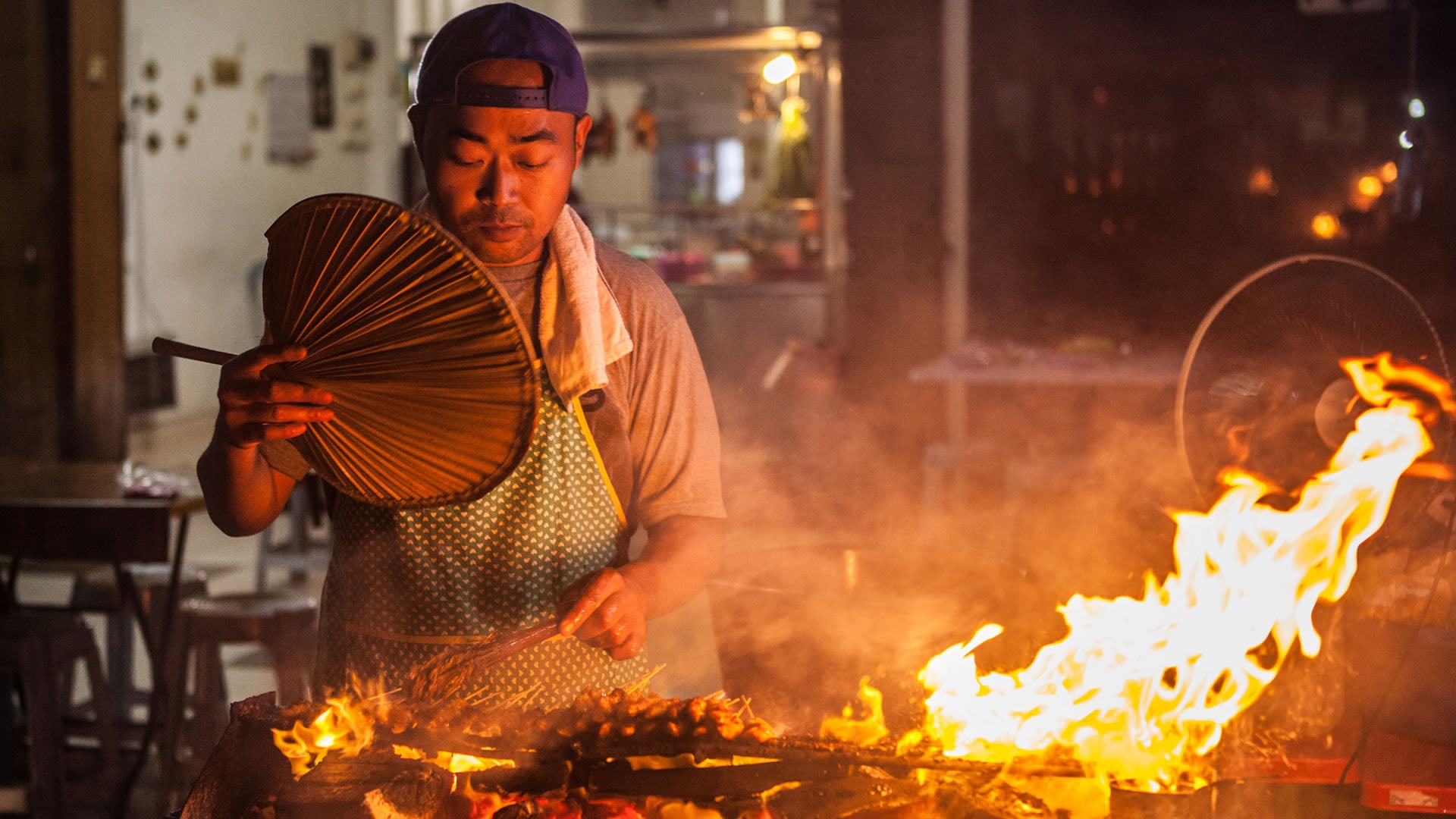 A man cooks satay chicken over an open grill in Malaysia.