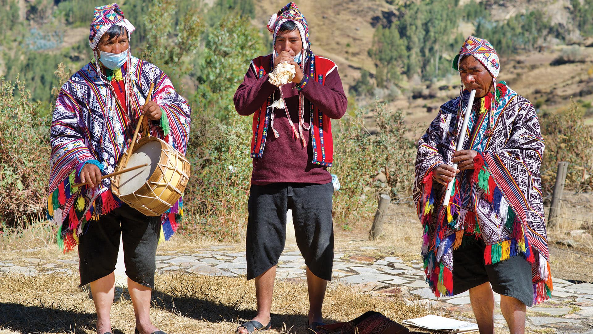 Three local musicians playing traditional Andean flutes and drums in colourful, traditional Cusco clothing
