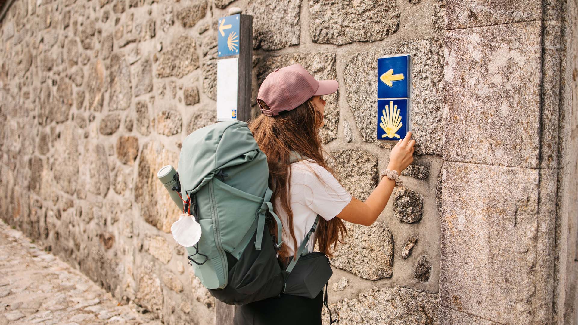 A woman hiking the Camino de Santiago in Spain touches one of the signposts along the trail.