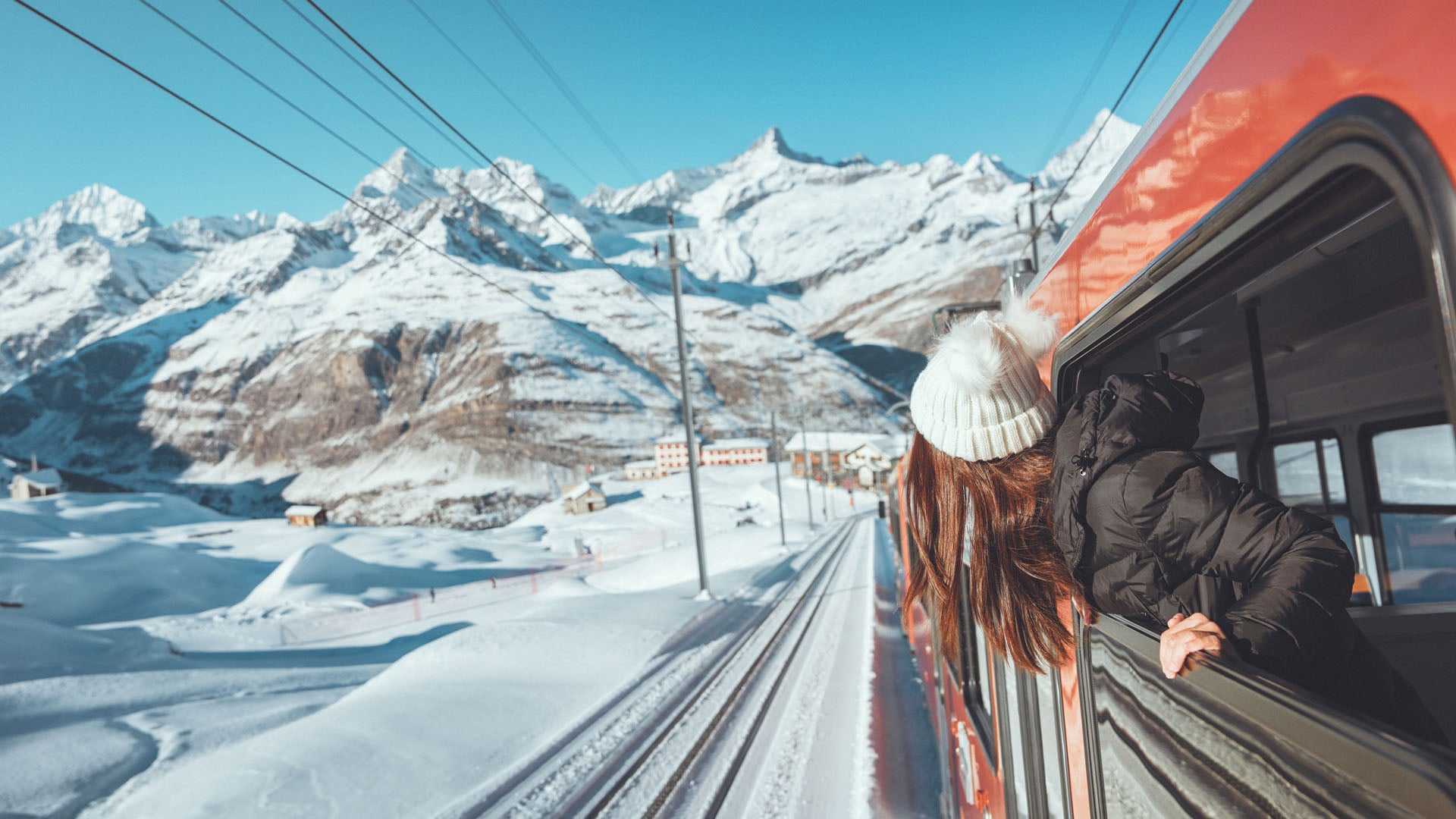 A woman sticking her head outside a window during winter on a train ride through Switzerland