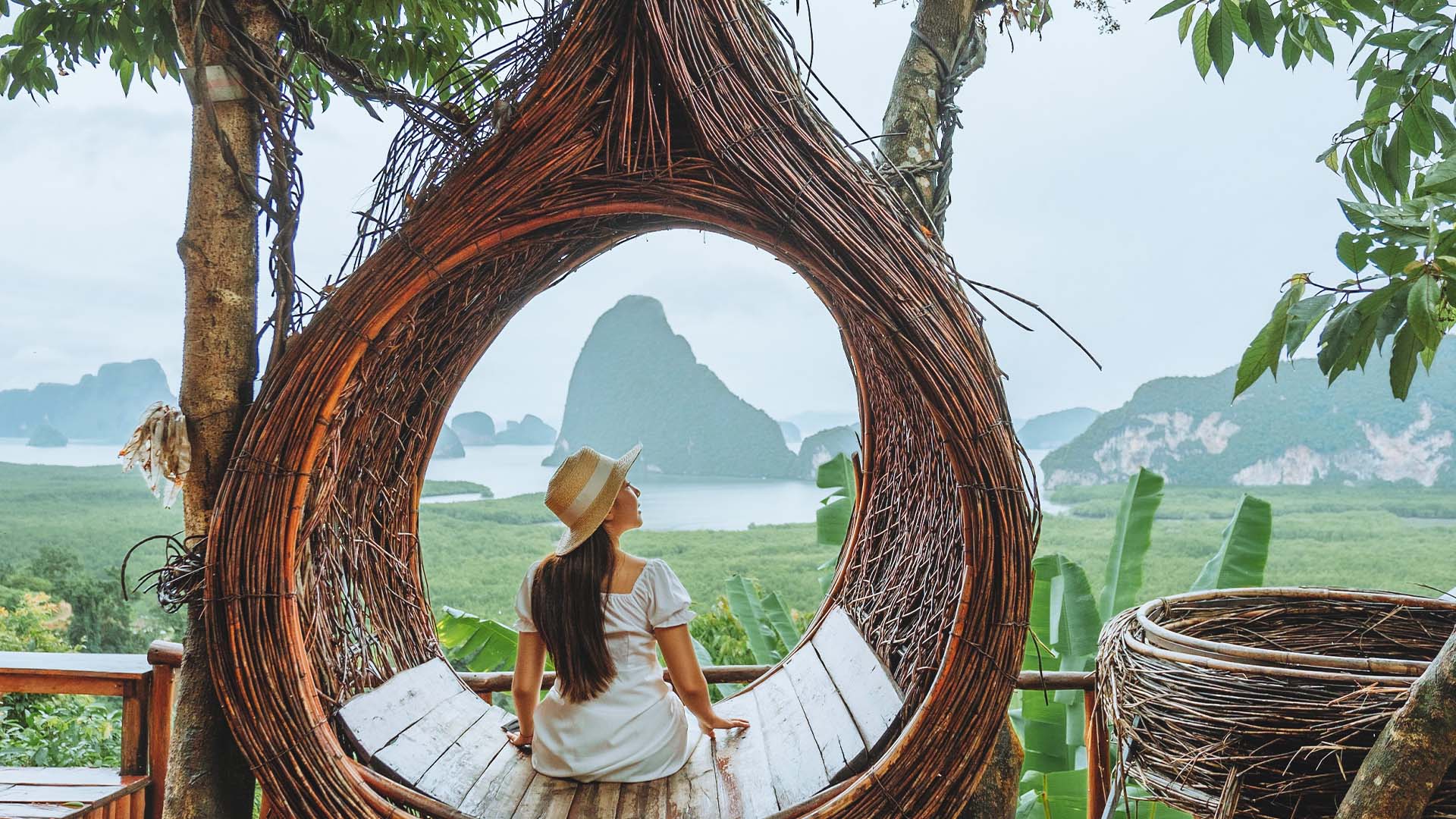 A woman sitting in a thatched wood hammock overlooking Phang Nga Bay in Thailand