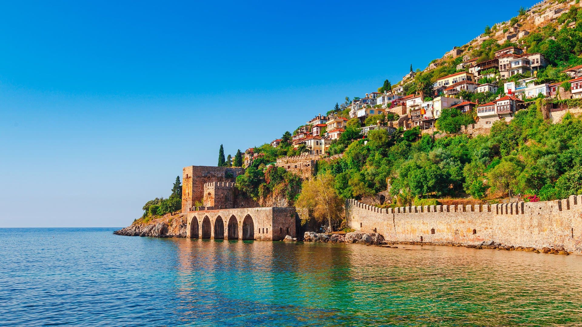 a sparkling coastline of homes cascading down to an old stone wall and tower in Antalya