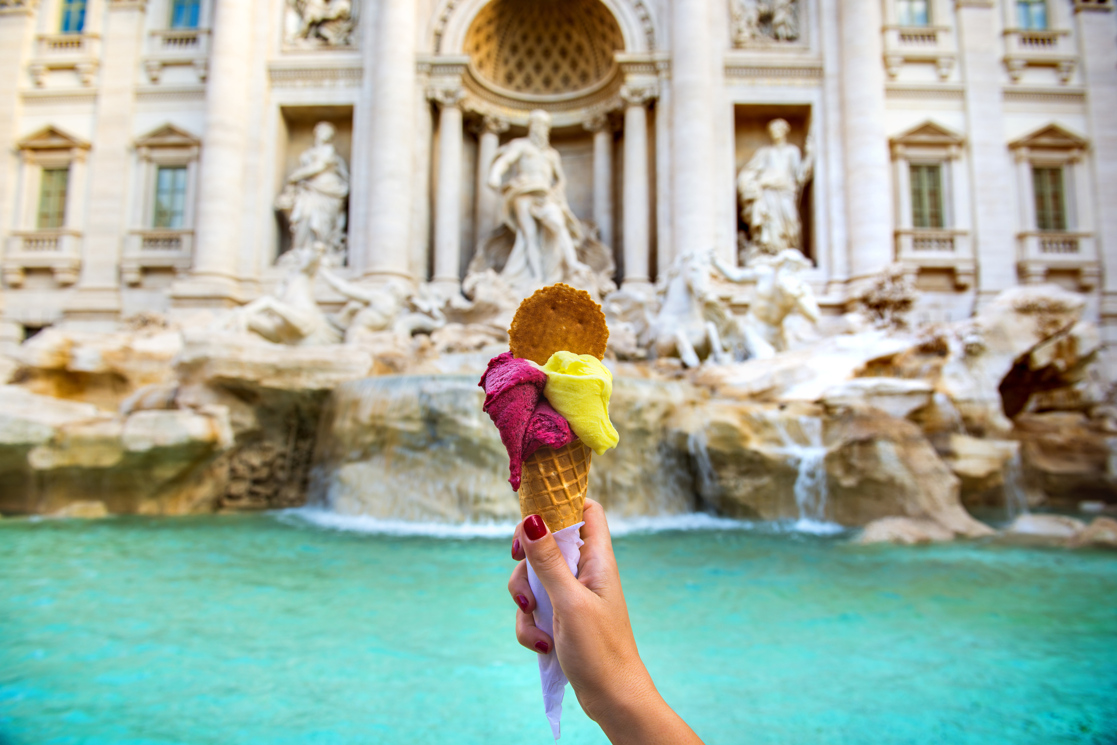 Hand holding colorful gelato in front of famous iconic Trevi Fountain at Rome, Italy.
