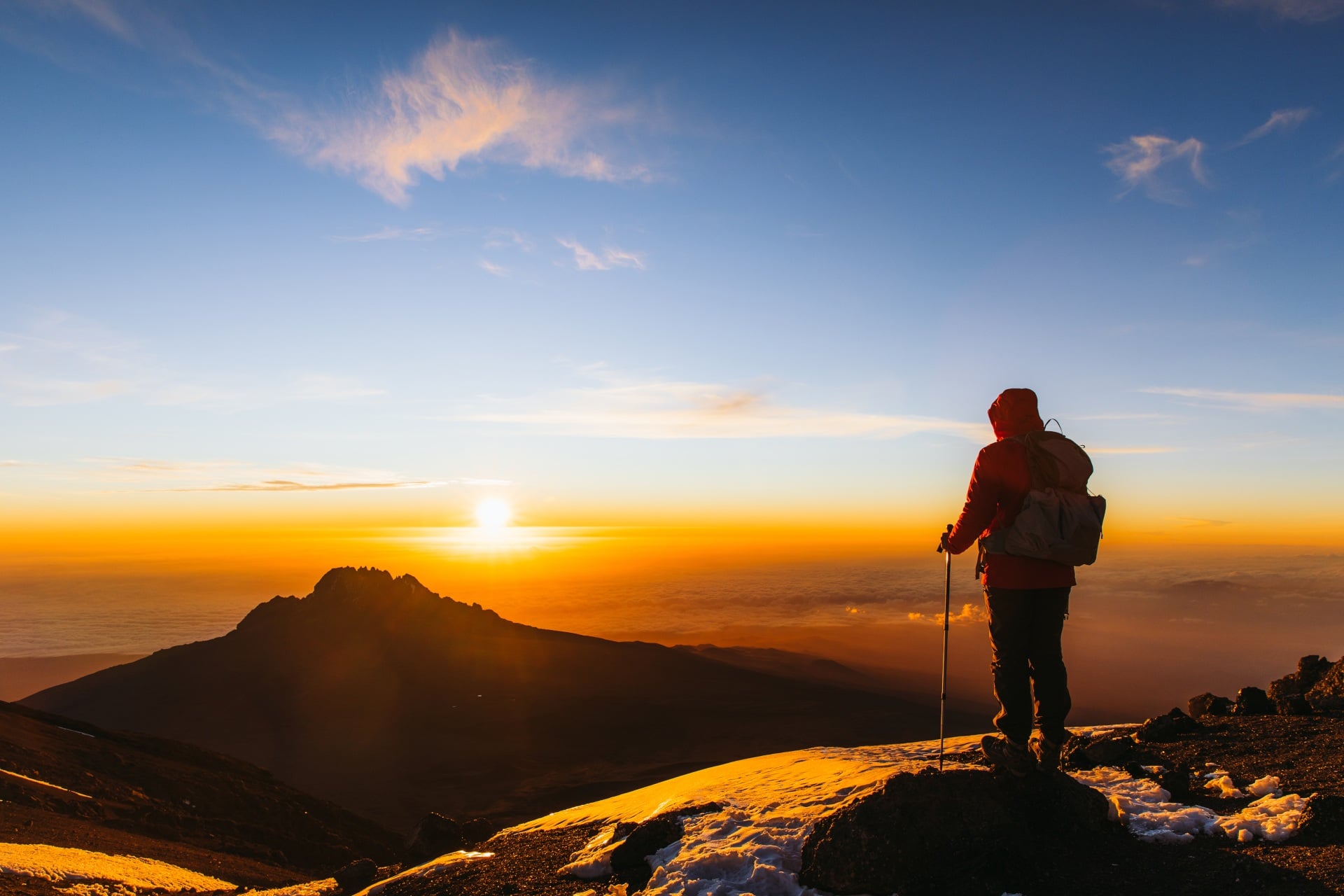 Man with backpack and hiking poles got to the top of Africa - Mount Kilimanjaro and looking at the beautiful bright sunny sunrise
