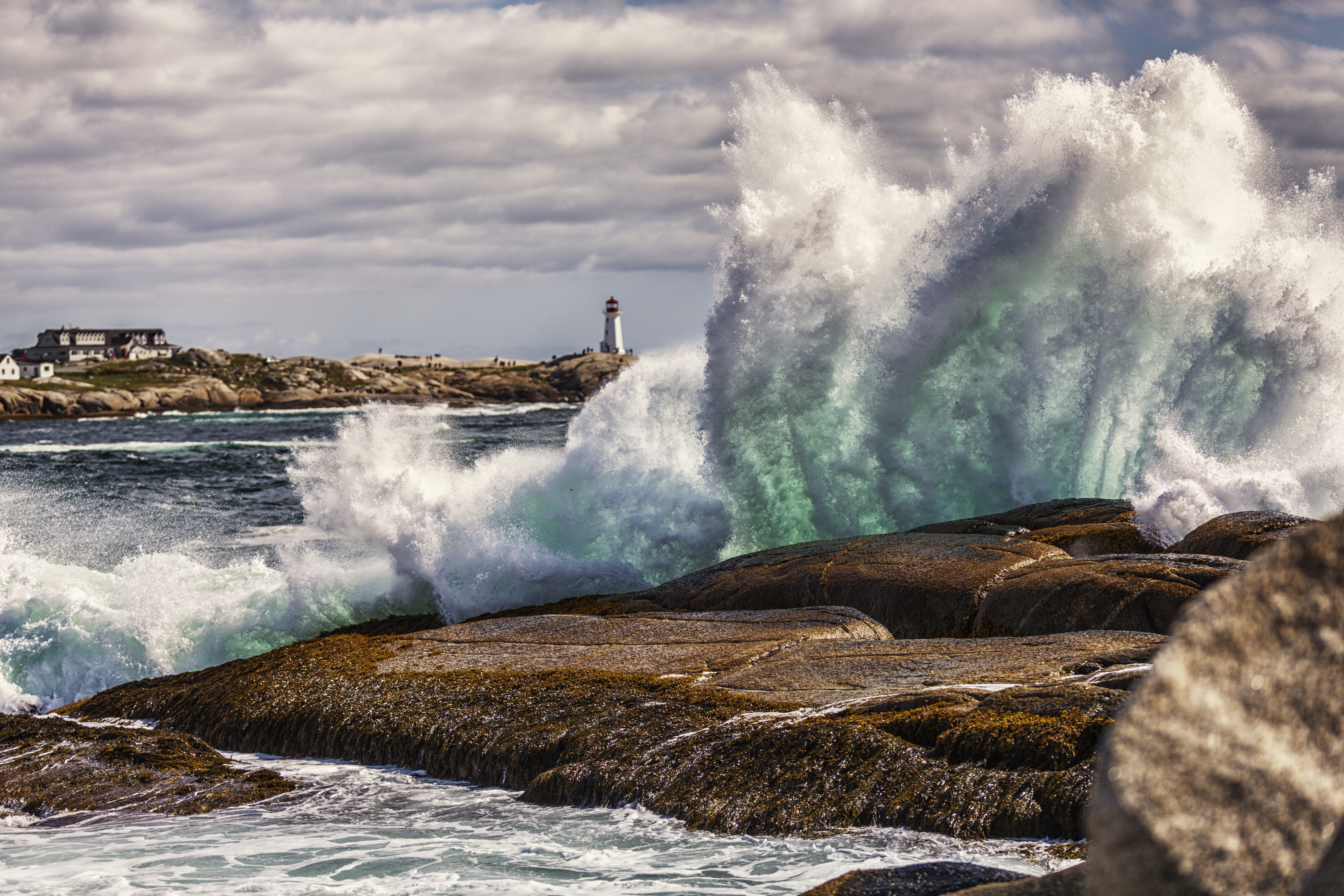 An offshore storm sends high, heavy, windswept ocean surf/breakers crashing up and over the coastal shoreline rocks at Peggy's Cove
