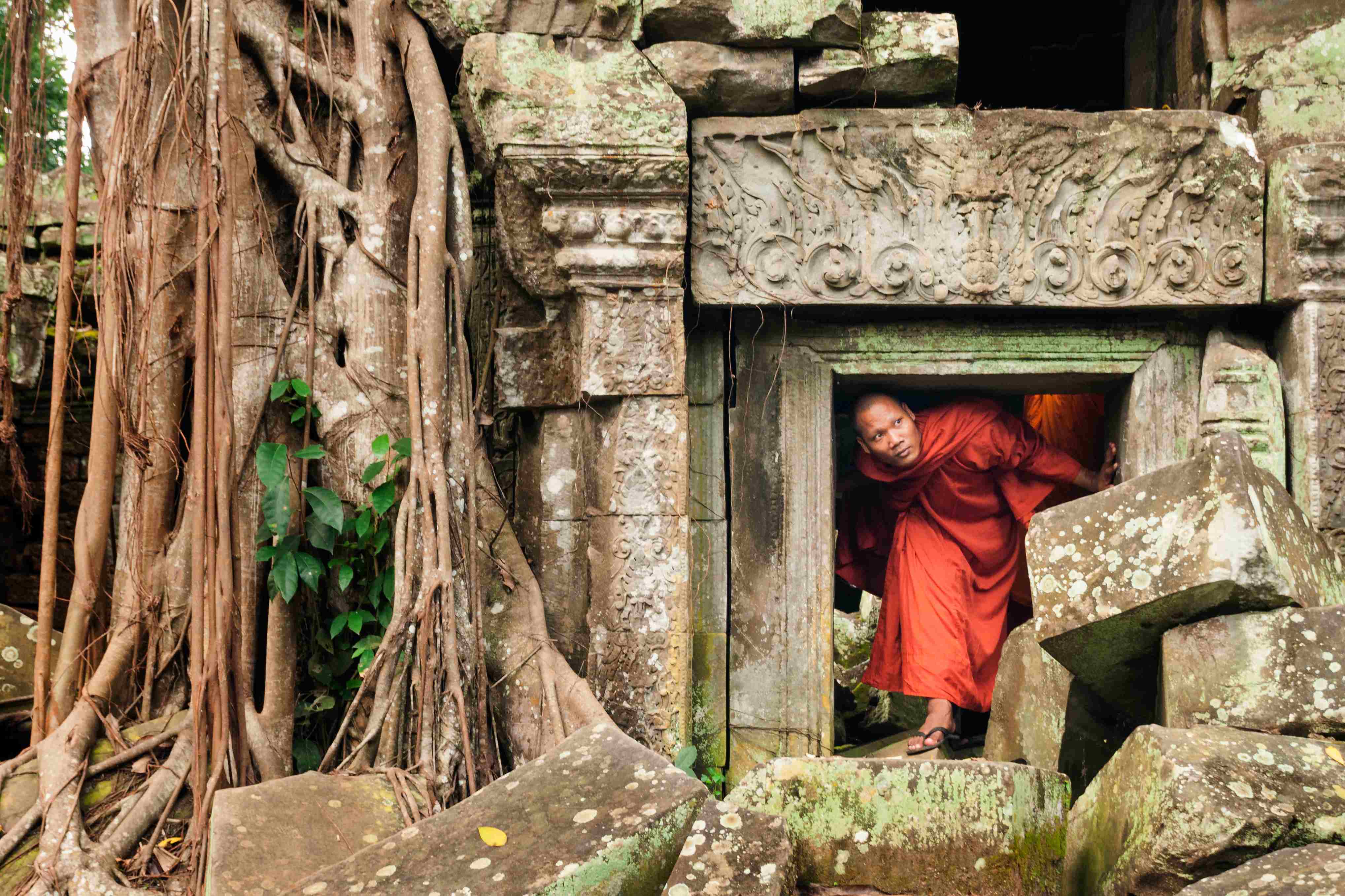 Cambodian monk ducks under a short doorway to explore an ancient temple