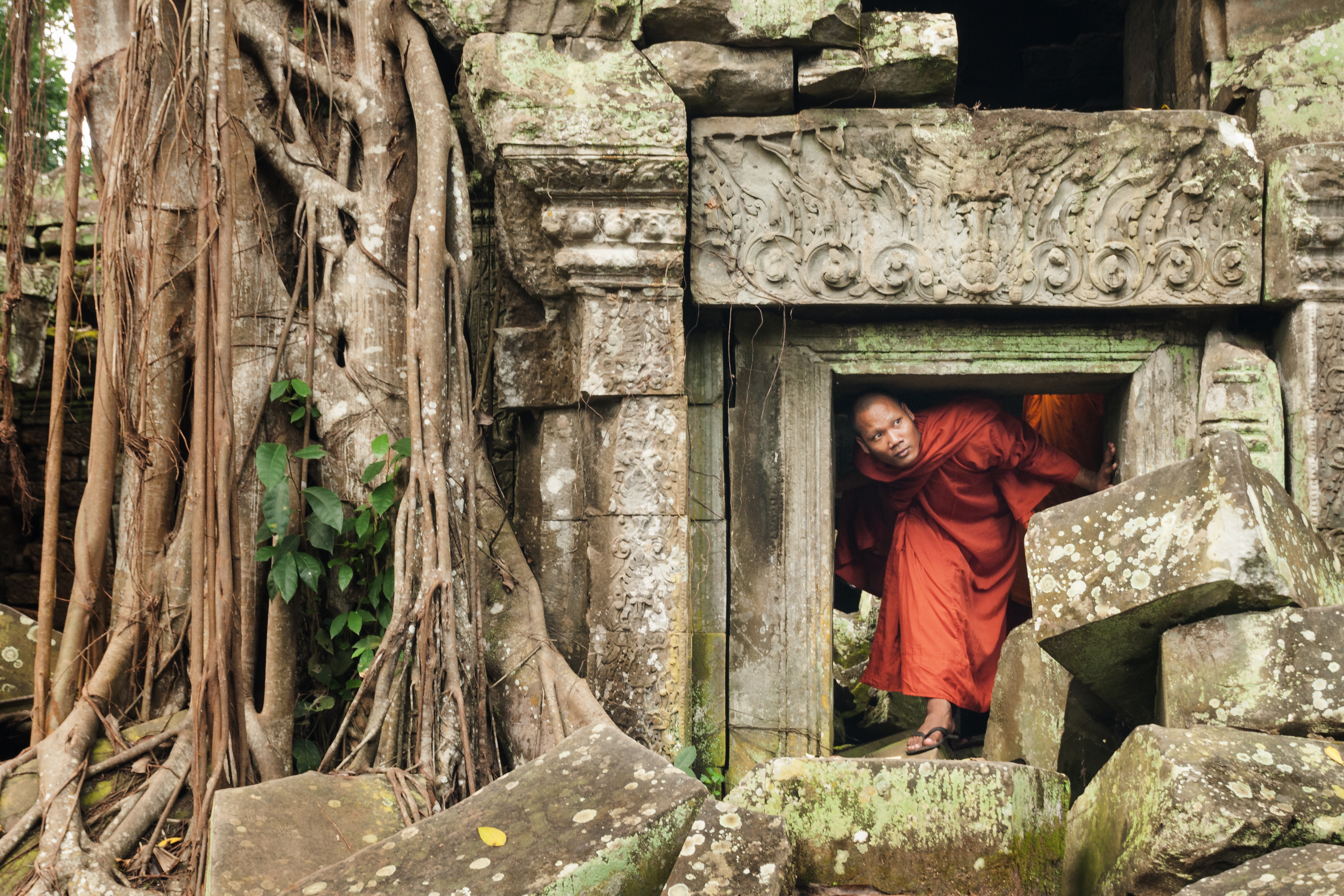 Cambodian monk ducks under a short doorway to explore an ancient temple