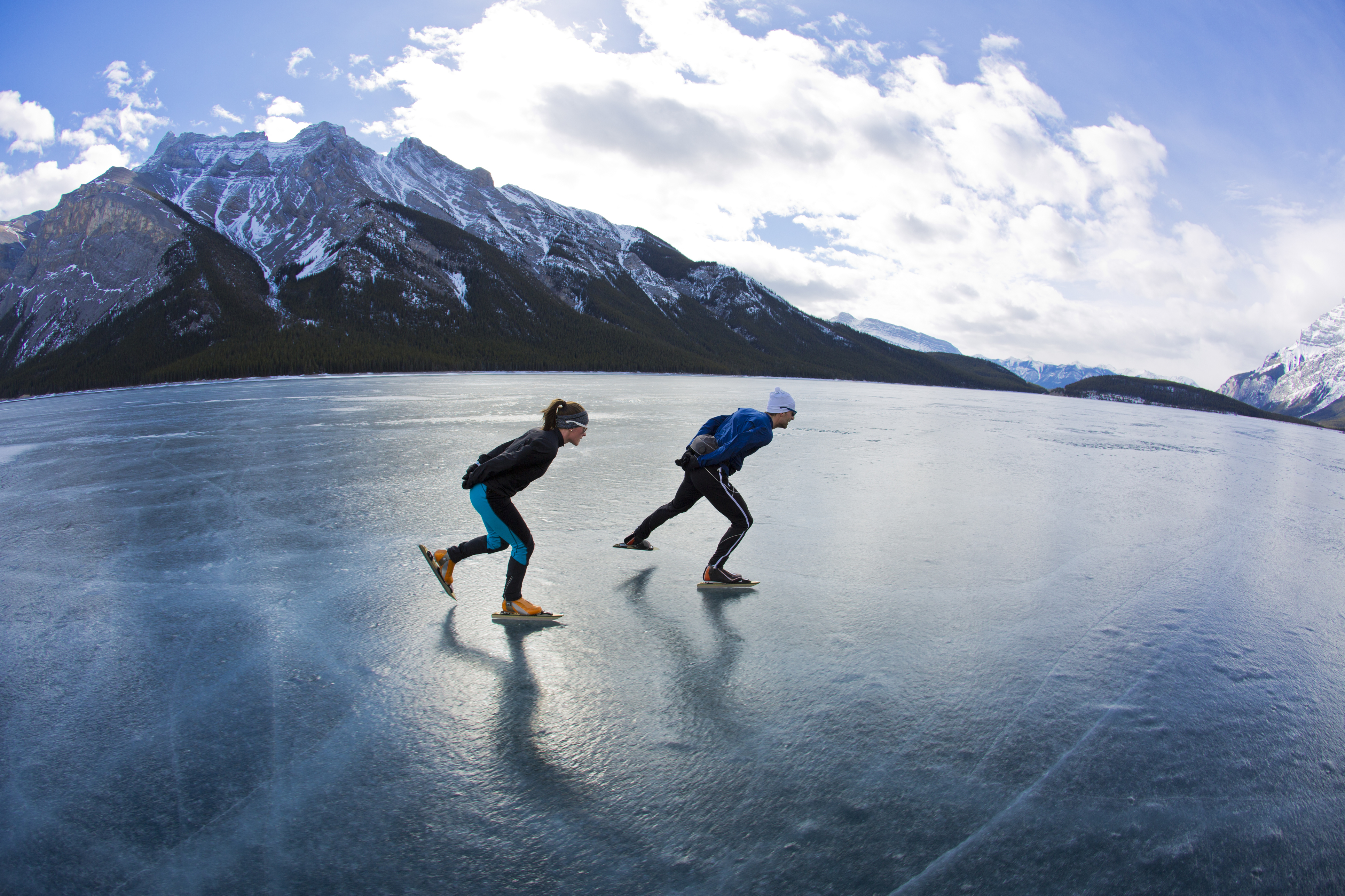A man leads a woman on a winter speed skating adventure on Lake Minnewanka in Banff National Park