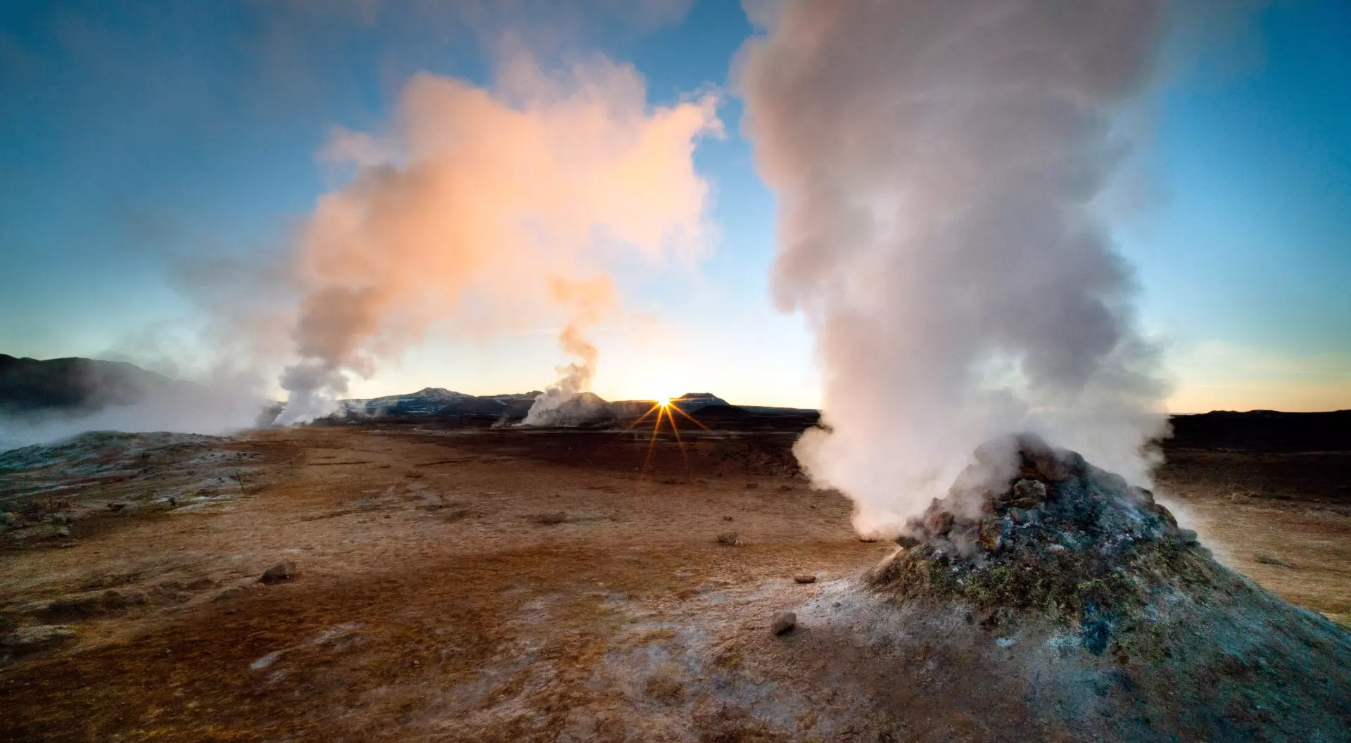 A beautiful dawn in Iceland, a country with many geothermal features including these dramatic fumaroles. Shot with a wide angle lens for dramatic effect and a small aperture to create a sunstar where the sun is just peaking over the horizon. The scenery in Iceland is spectacular and it is becoming a popular tourist destination.