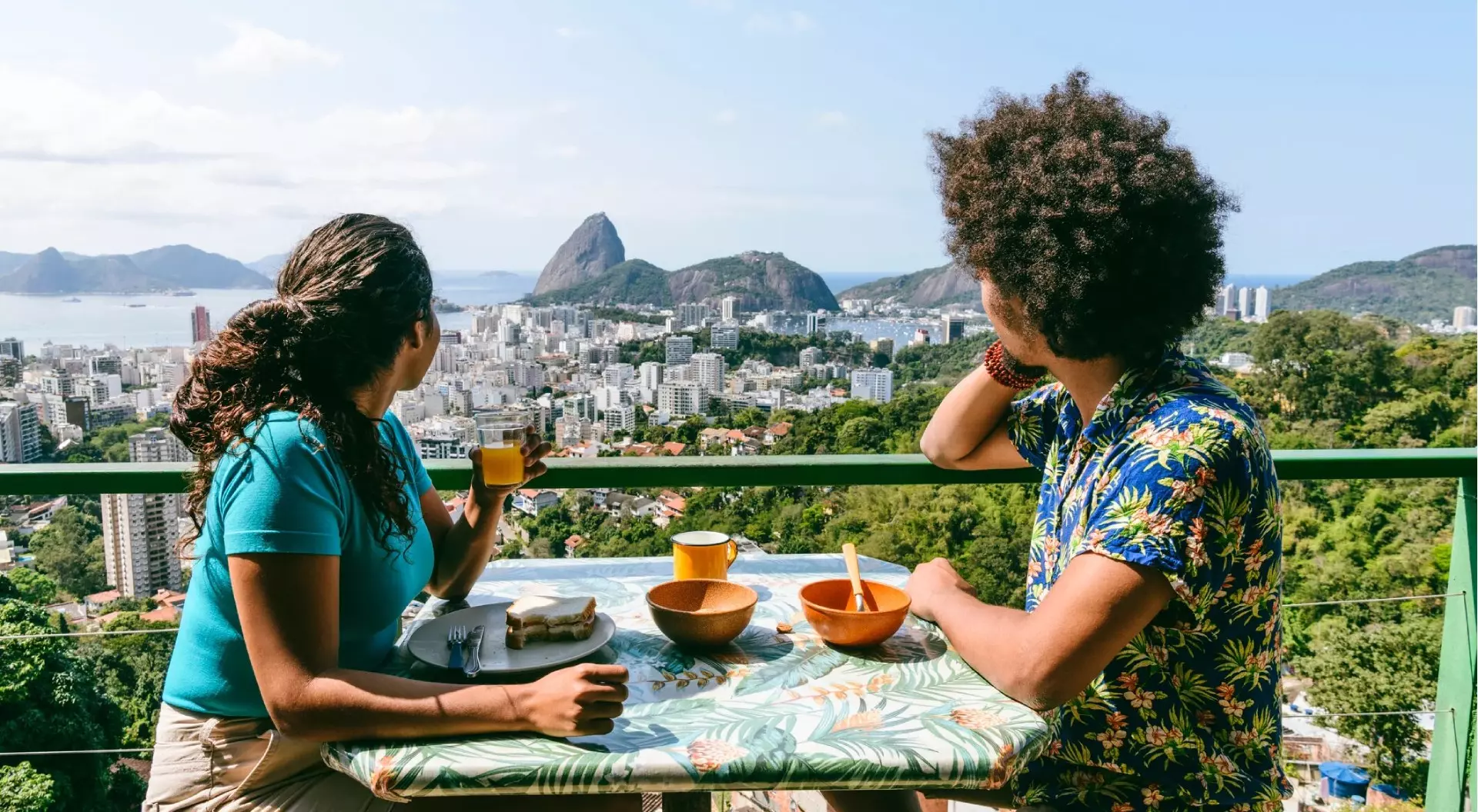 A couple on holiday enjoying a meal in Rio de Janeiro, Brazil, overlooking Sugarloaf mountain from an outdoor rooftop cafe.