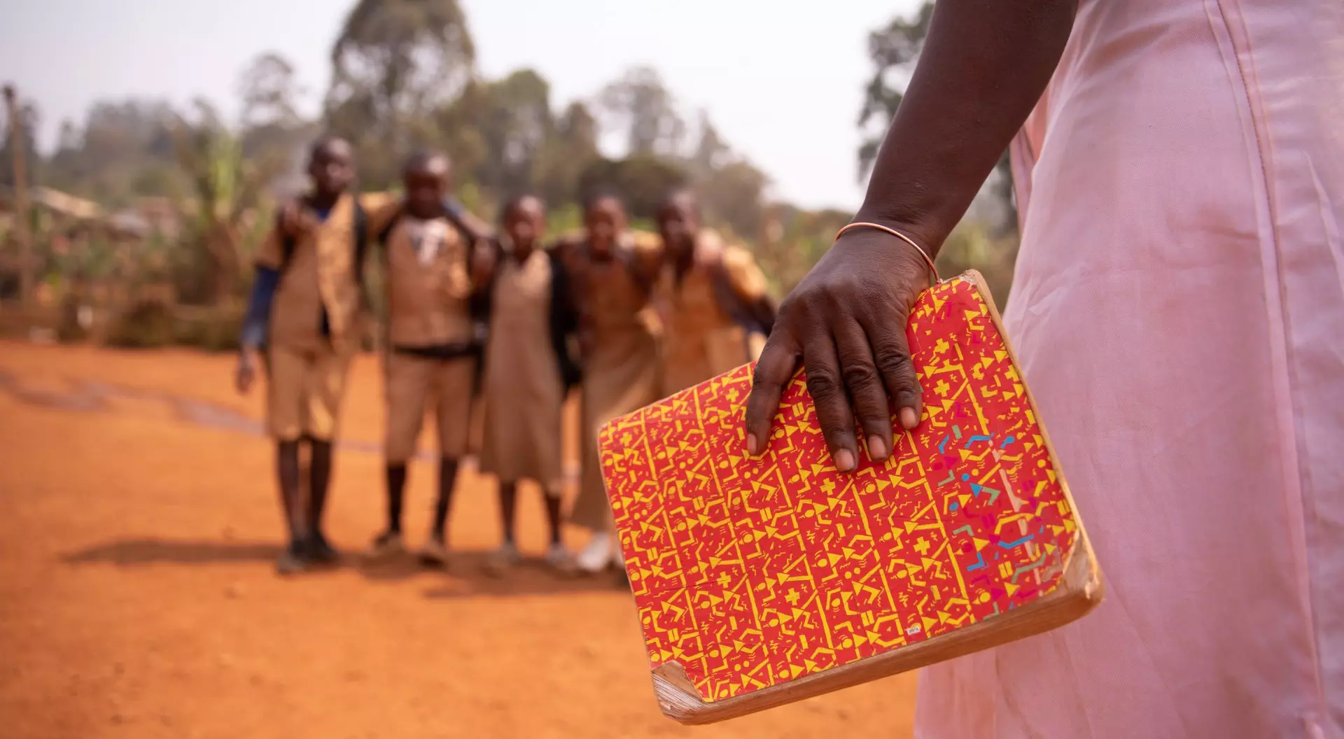 An african teacher is holding a book with her students out of focus in the background