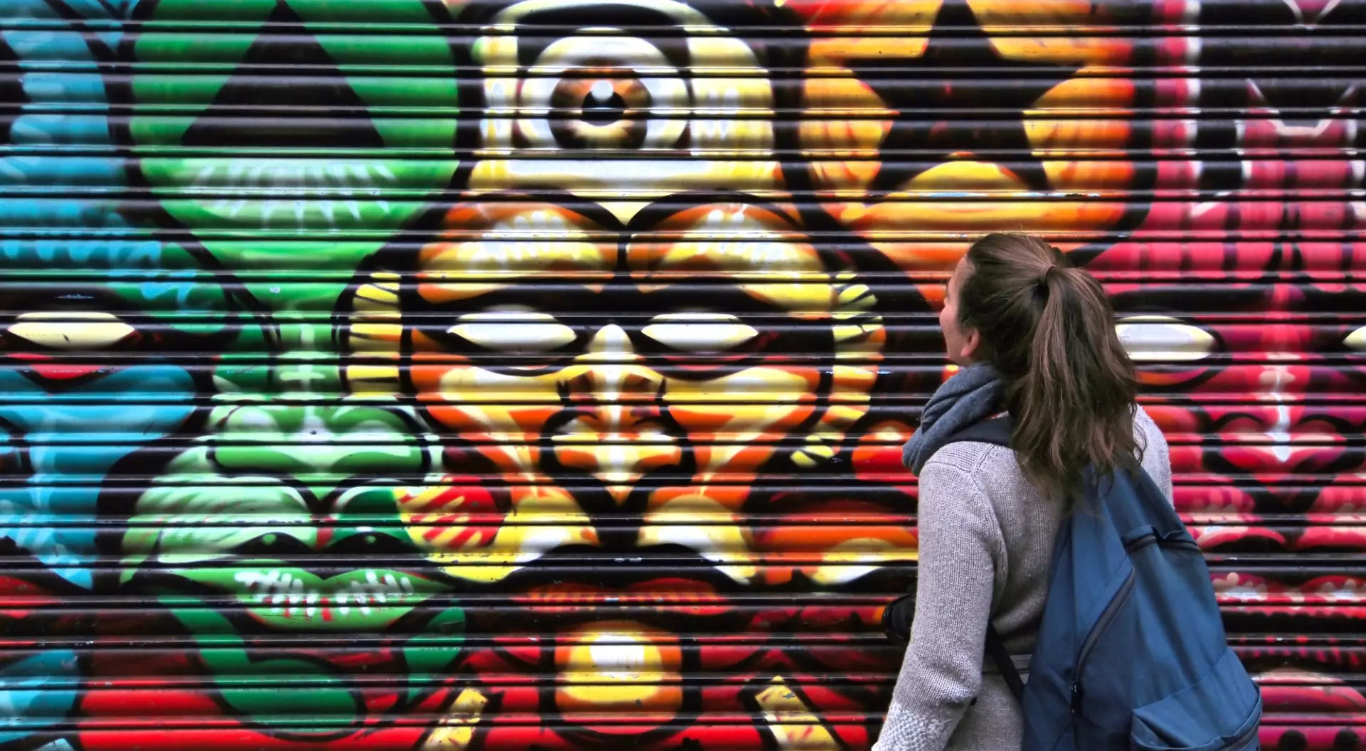 London, England Back view of a Lady looking at roll-up door, painted with colorful graffiti, representing figures like ancient swings, stars and light.