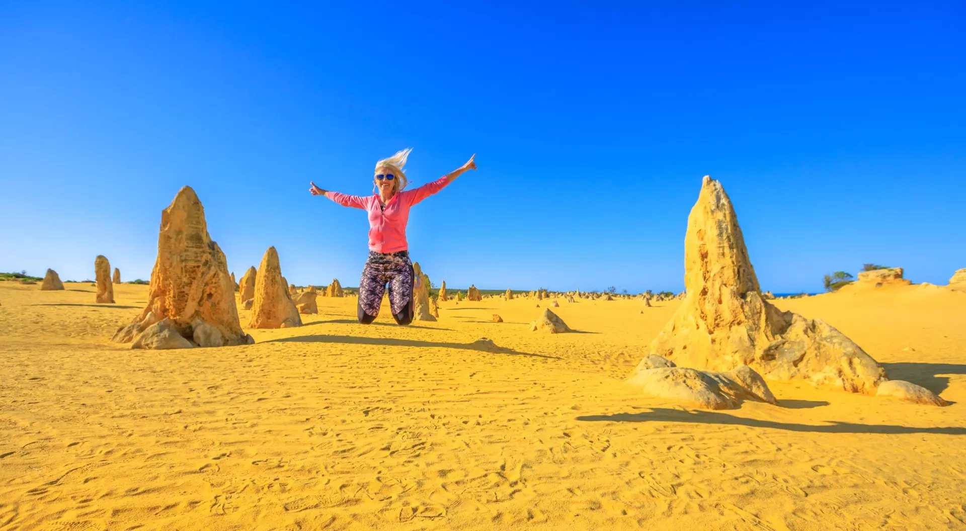 Blond girl jumping in the Pinnacles desert of Nambung National Park, Western Australia, Australia