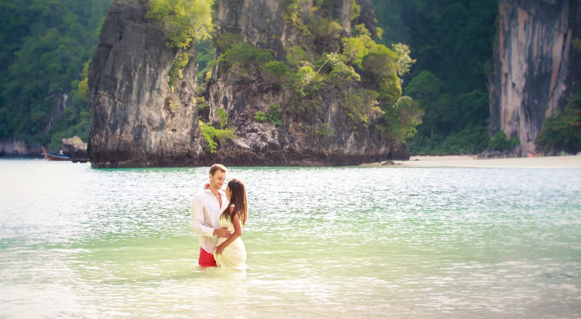 Thailand Couple stand in sea water in island bay with karst in background, Thailand