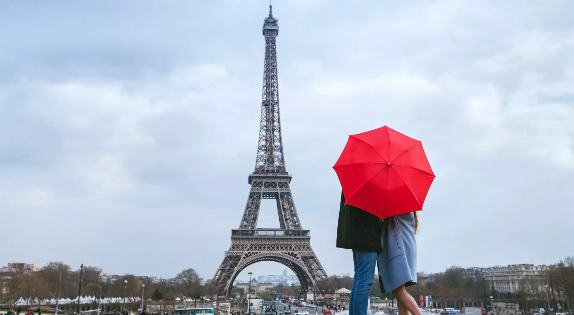Honeymoon in Paris, Couple kissing behind red umbrella against Eiffel Tower, France
