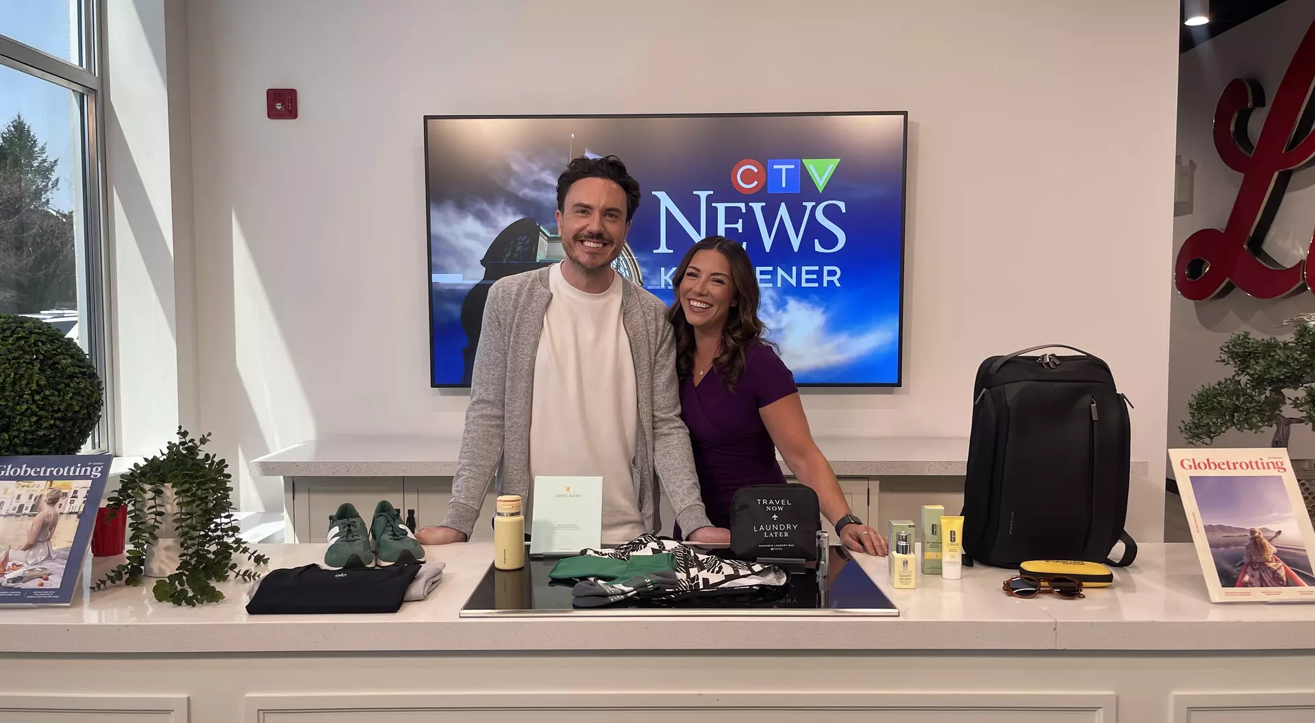 Mitchell Fawcette, Editor-in-Chief of Globetrotting Magazine, and Leighanne Evans of CTV KW Evening News in Kitchener smiling before their local news segment.