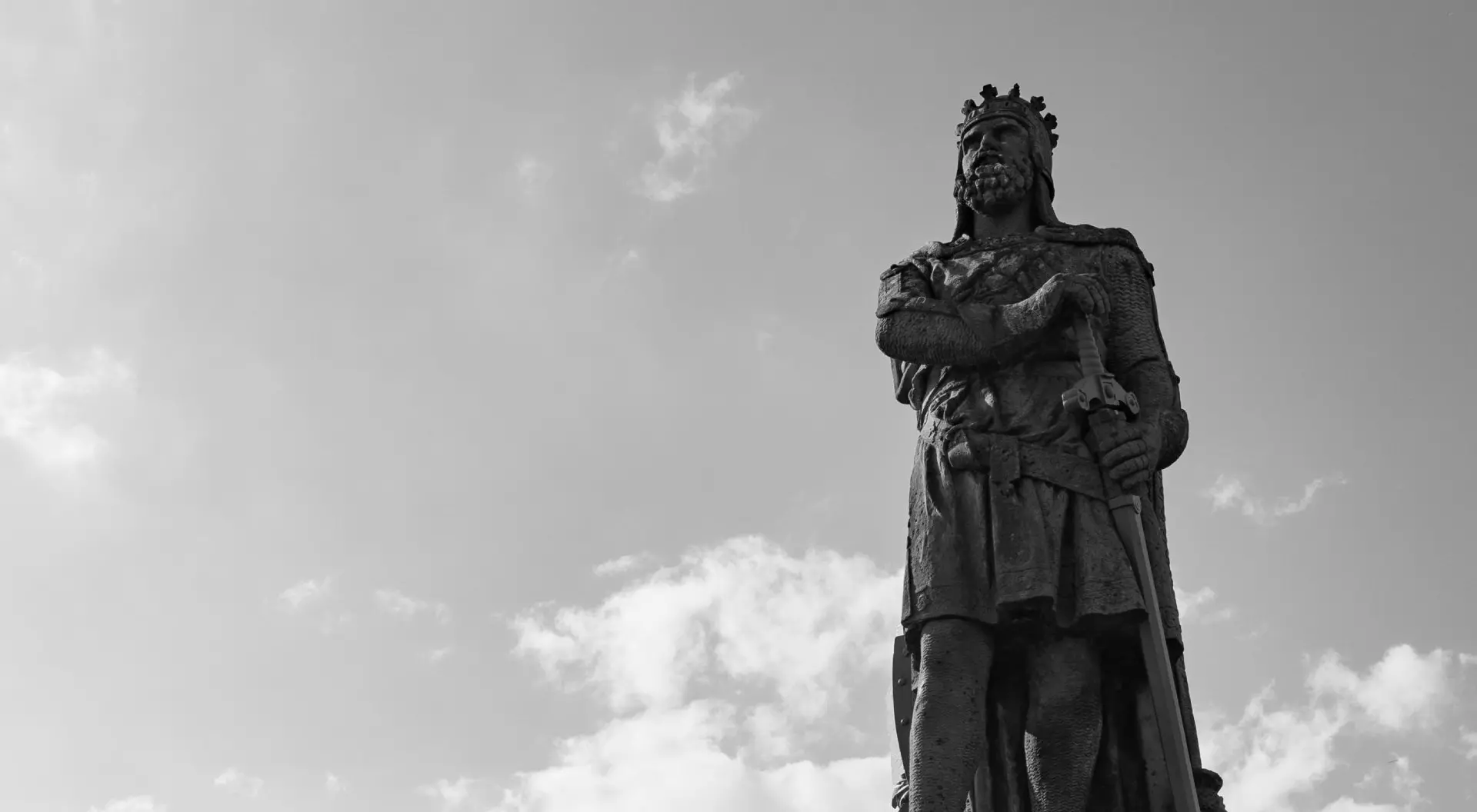 Low angle shot of the statue of Robert the Bruce under a cloudy sky in grayscale