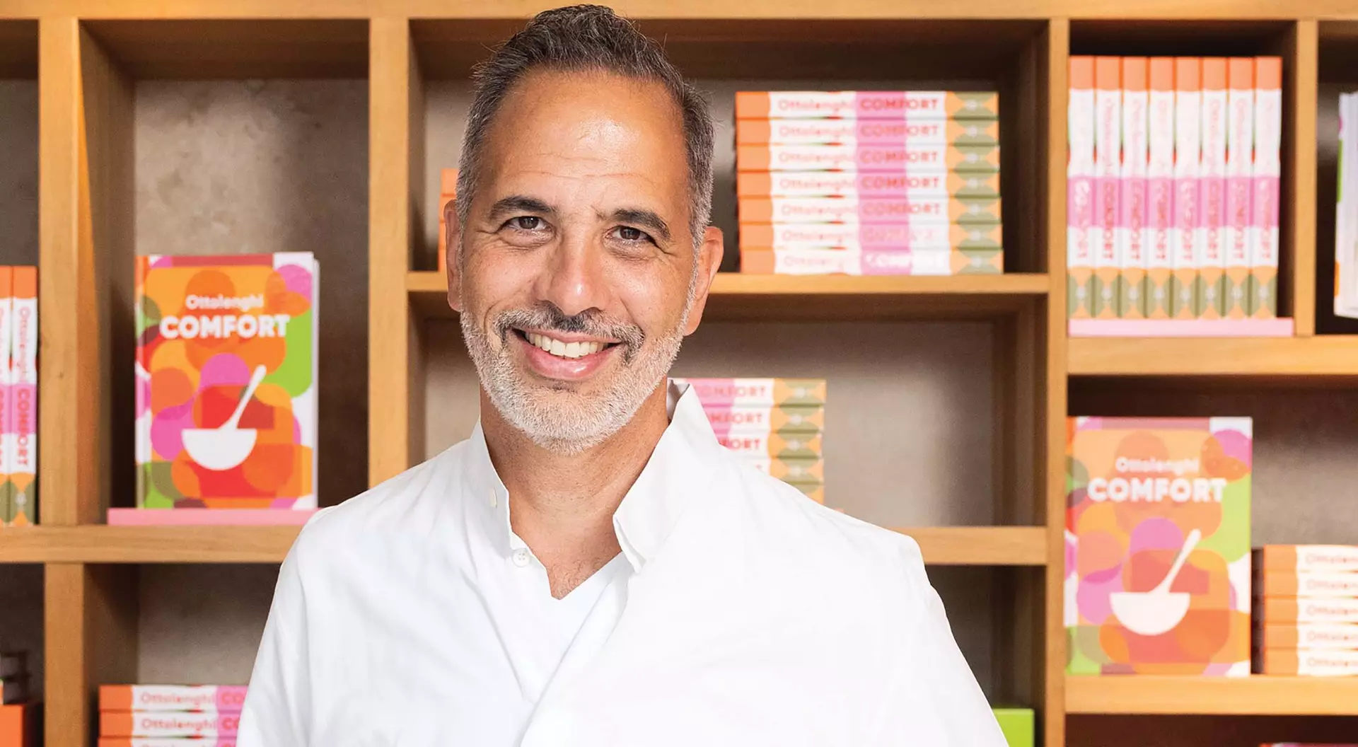Chef Yotam Ottolenghi poses in front of copies of his newest book, Comfort