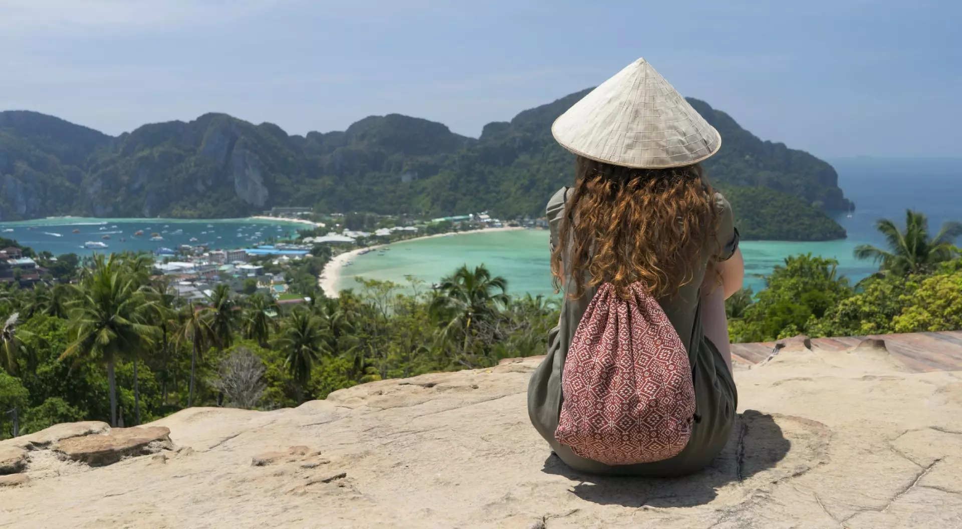 Rear view of a female tourist sitting at the Phi Phi viewpoint and looking on a sandbar.