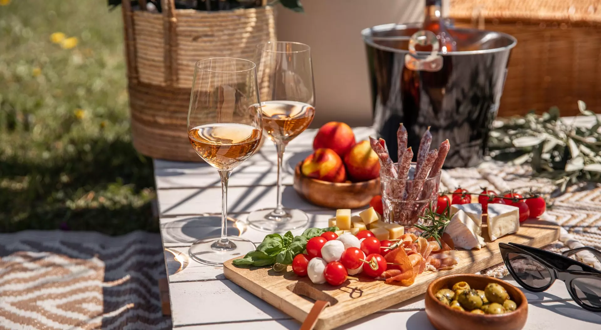 Rose wine glasses with antipasti picnic food snacks on sunny garden party table