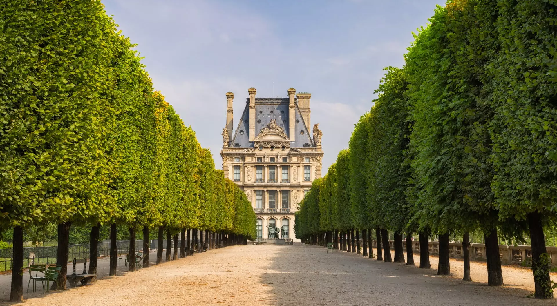 Summer morning view of Tuilleries garden in Paris, France. Tree-lined path leads to the south west facade of the Louvre Museum.