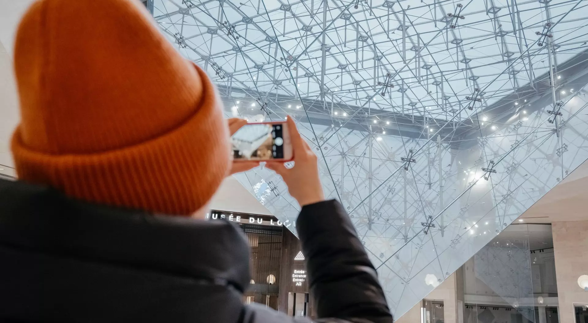 Paris, France Young woman taking a photo. Inverted pyramid in the shopping mall 'Carrousel du Louvre' with people in Paris, France