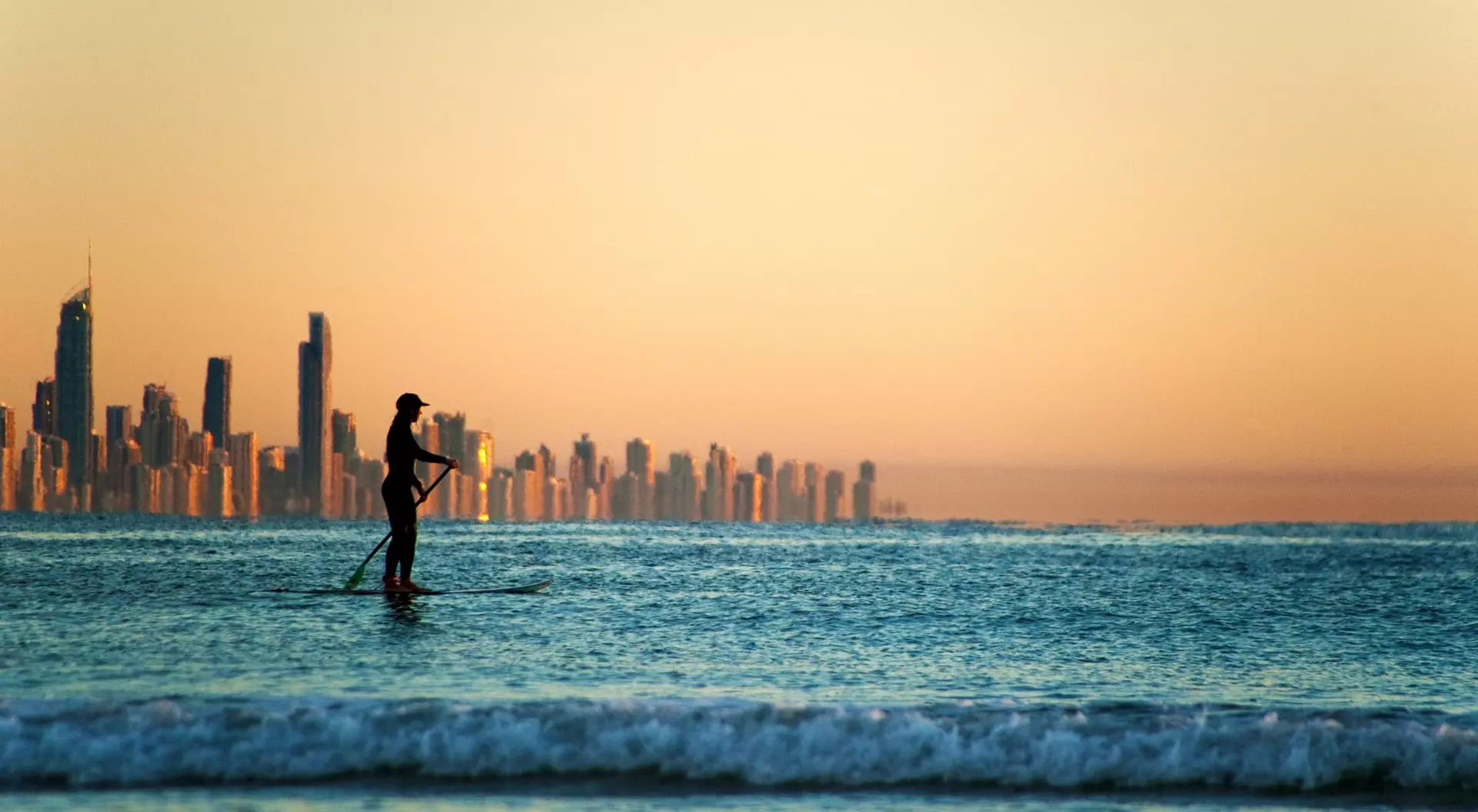 person on paddleboard off coast with city in background