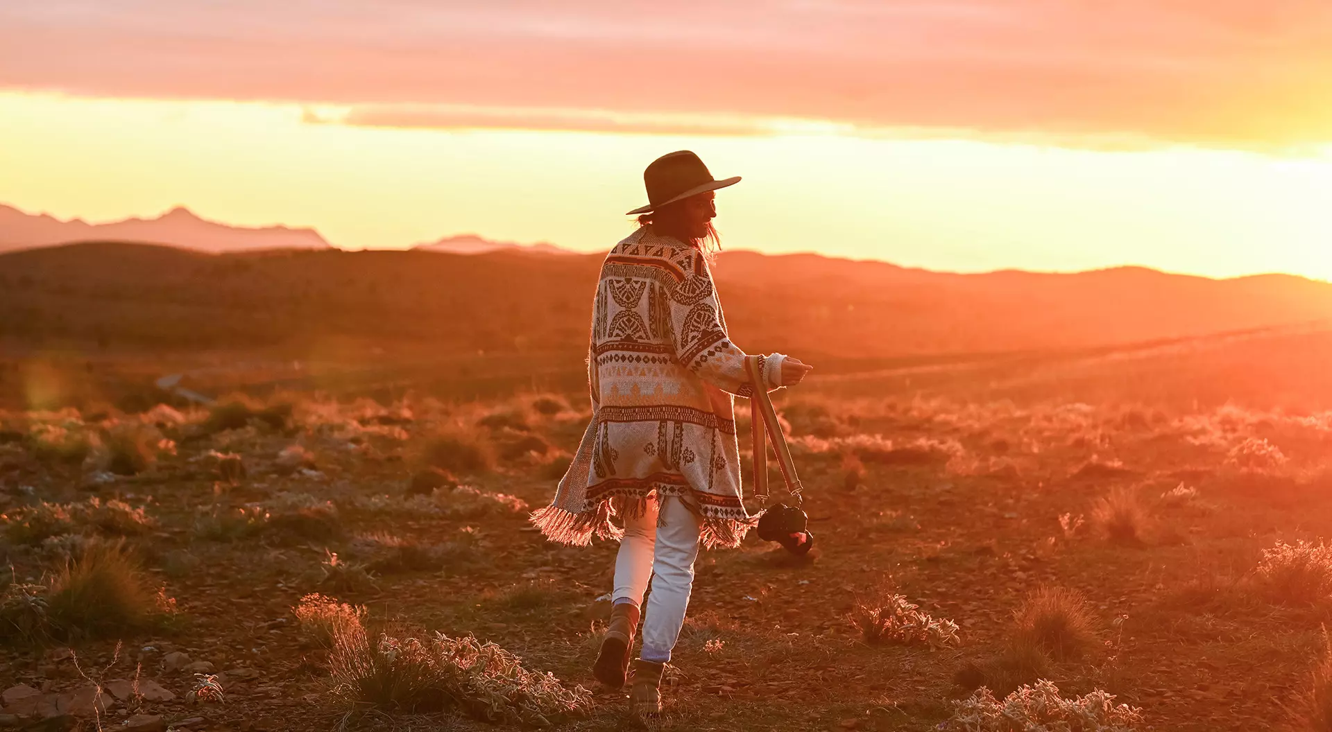 A woman with a camera walking through the Australian outback underneath a red glow from the sun