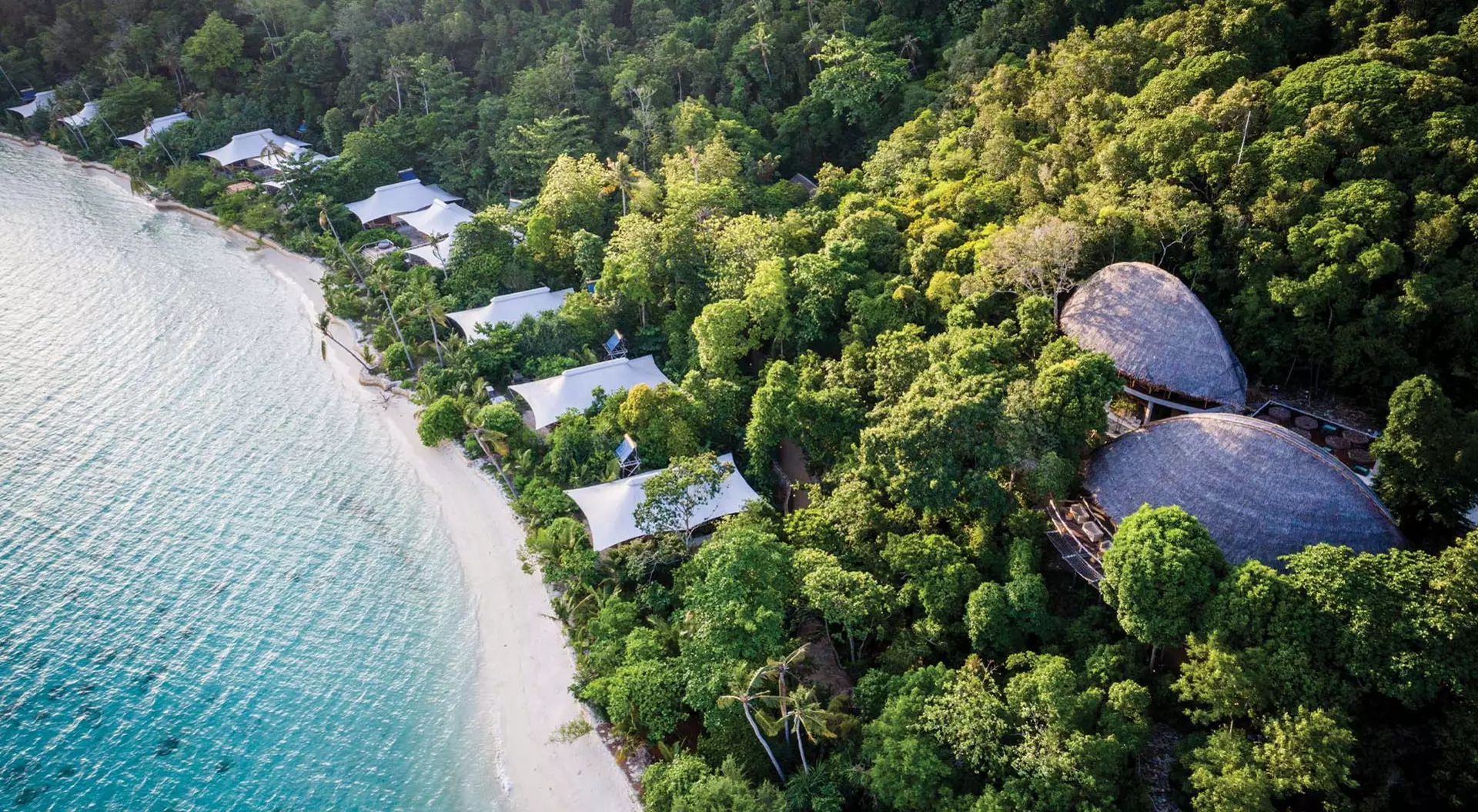 Aerial view of the west beach suites in a green forest at Bawah Reserve in Indonesia