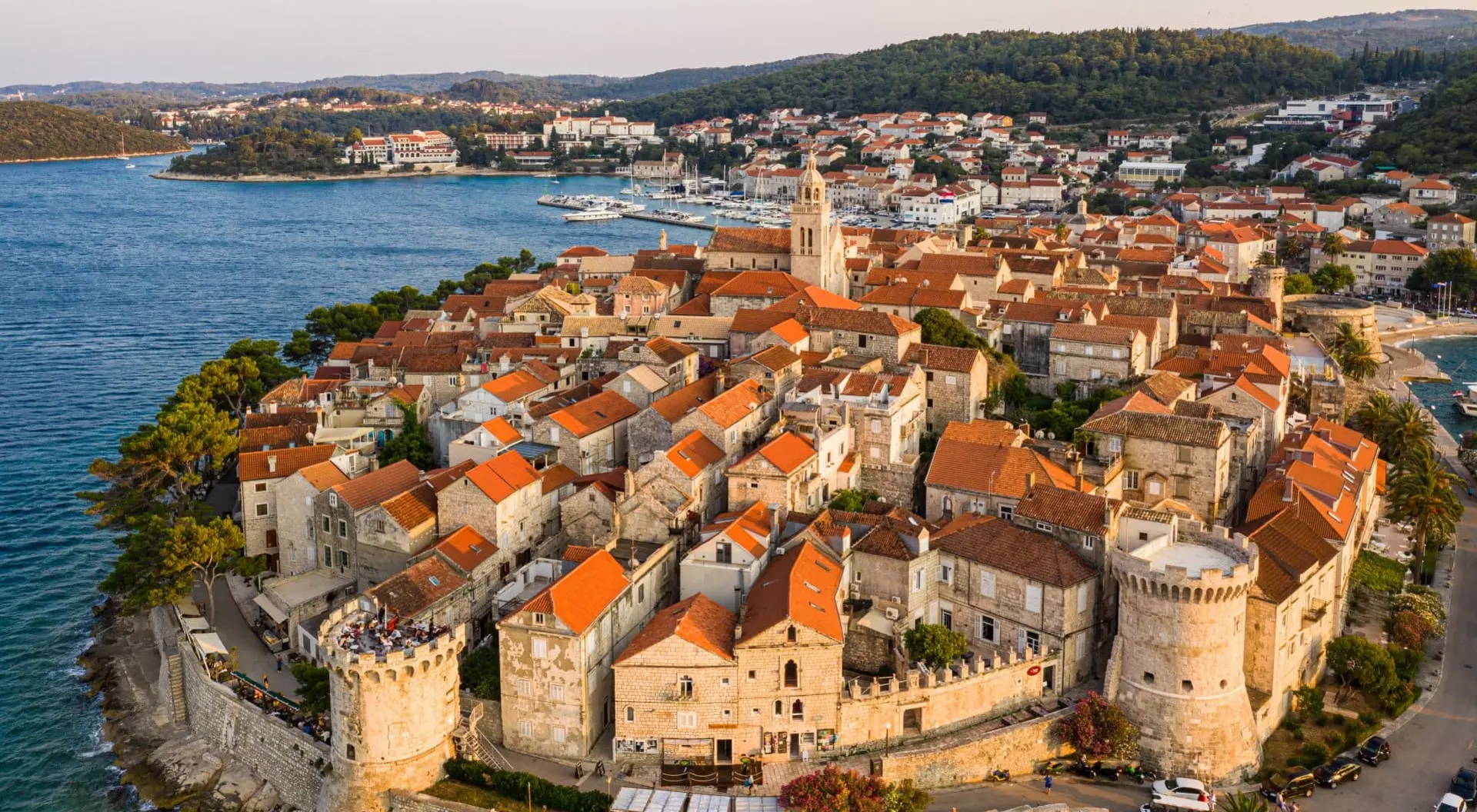 an aerial view of red-roofed homes and medieval walls surrounding the Croatian city of Korcula