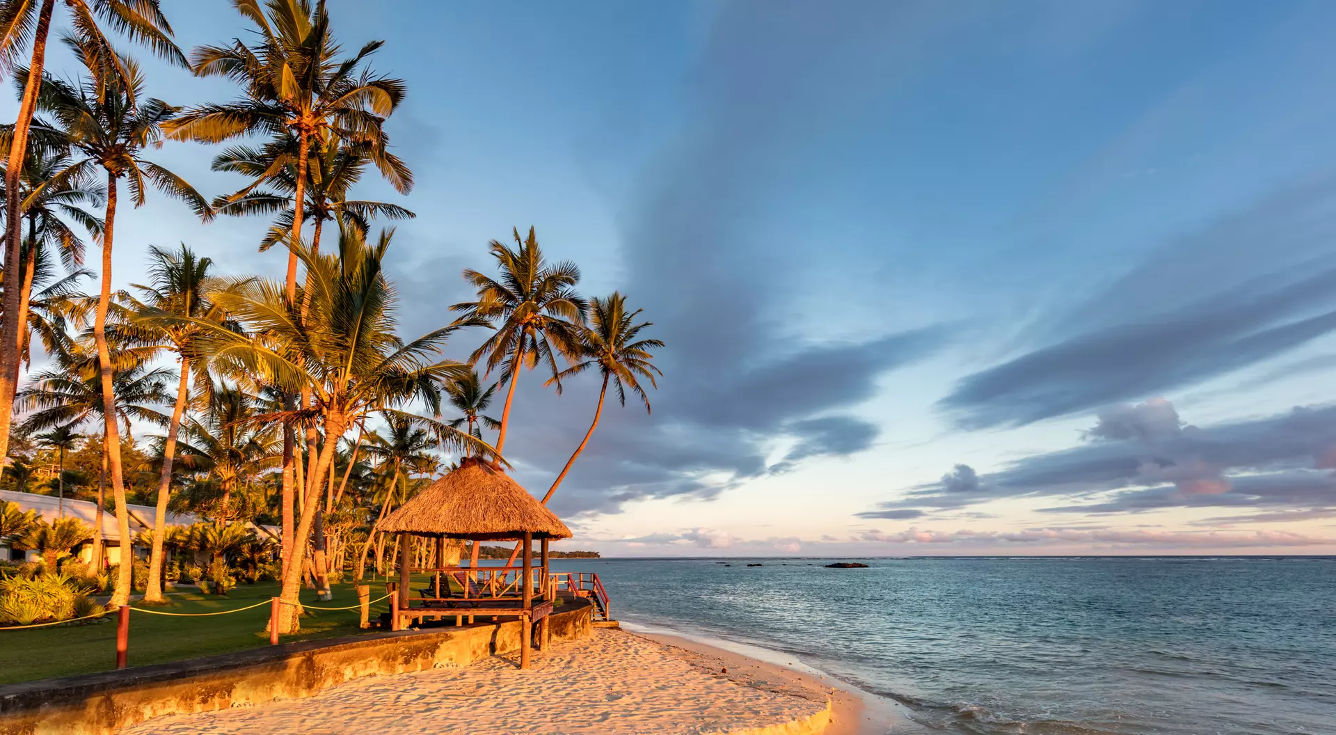 A beach on Fiji's Coral Coast at sunset, with the palm trees swaying and the ocean breeze sweeping through the island.