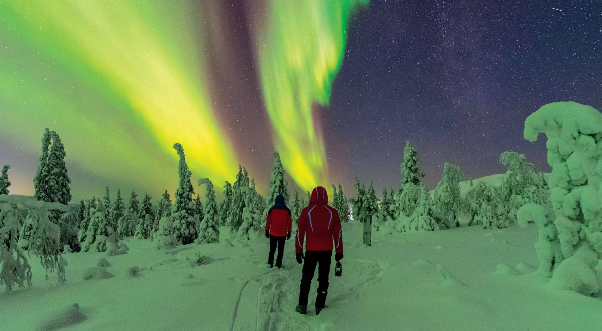 Two walkers watch the Northern Lights in winter in far northern Finnish Lapland.