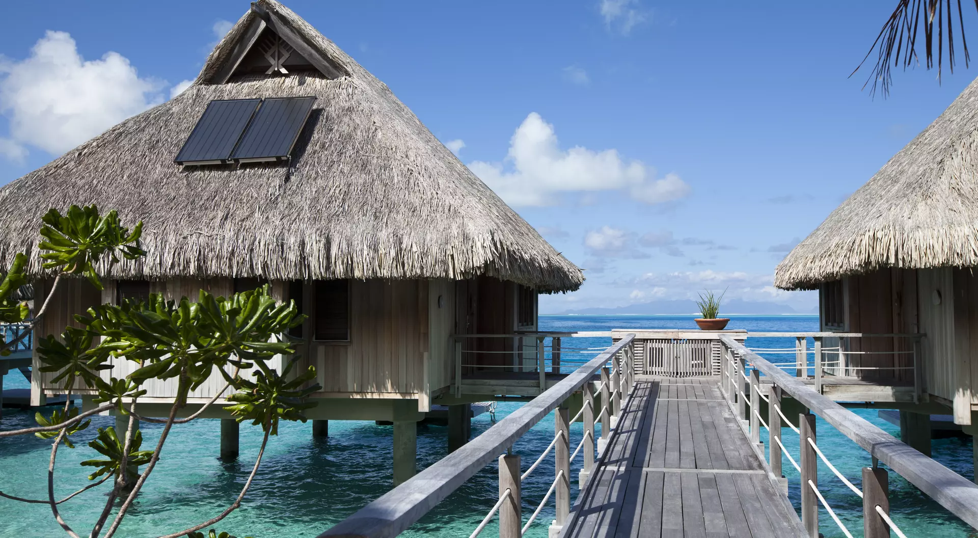 Wooden walkways over the water of the blue tropical sea to authentic traditional Polynesian thatched roof houses with eco-friendly use of solar panels. Polynesia, Tahiti