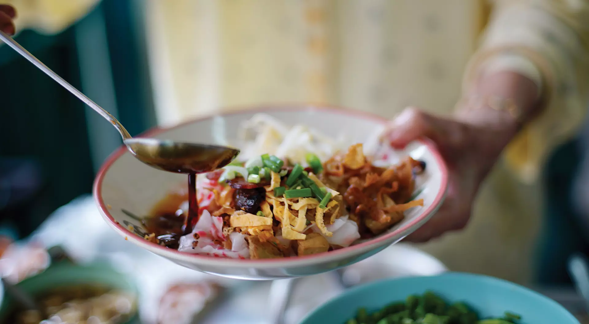 Merchant cook soy sauce on top of delicious Chinese steamed rice noodle rolls, beautifully arranged in white plate ready to serve customer in local restaurant in Thailand