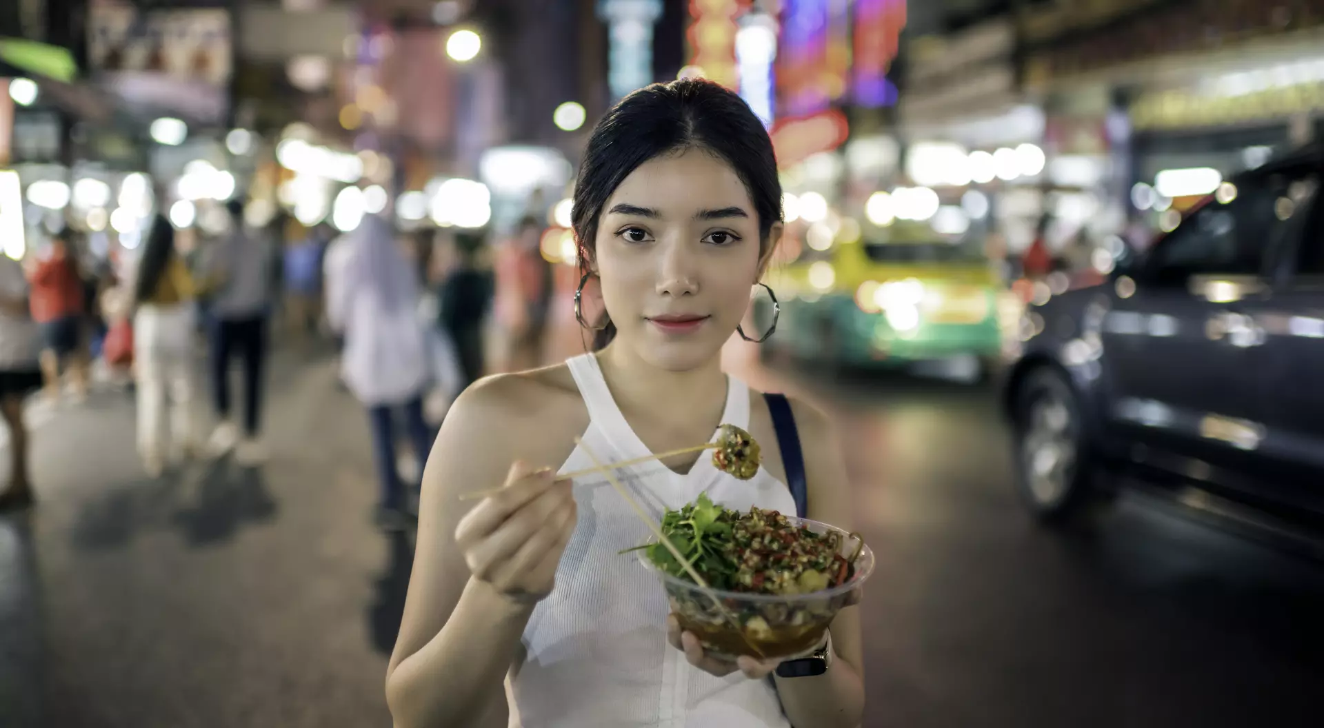 young woman eating grilled squid in Chinatown, Bangkok, Thailand.