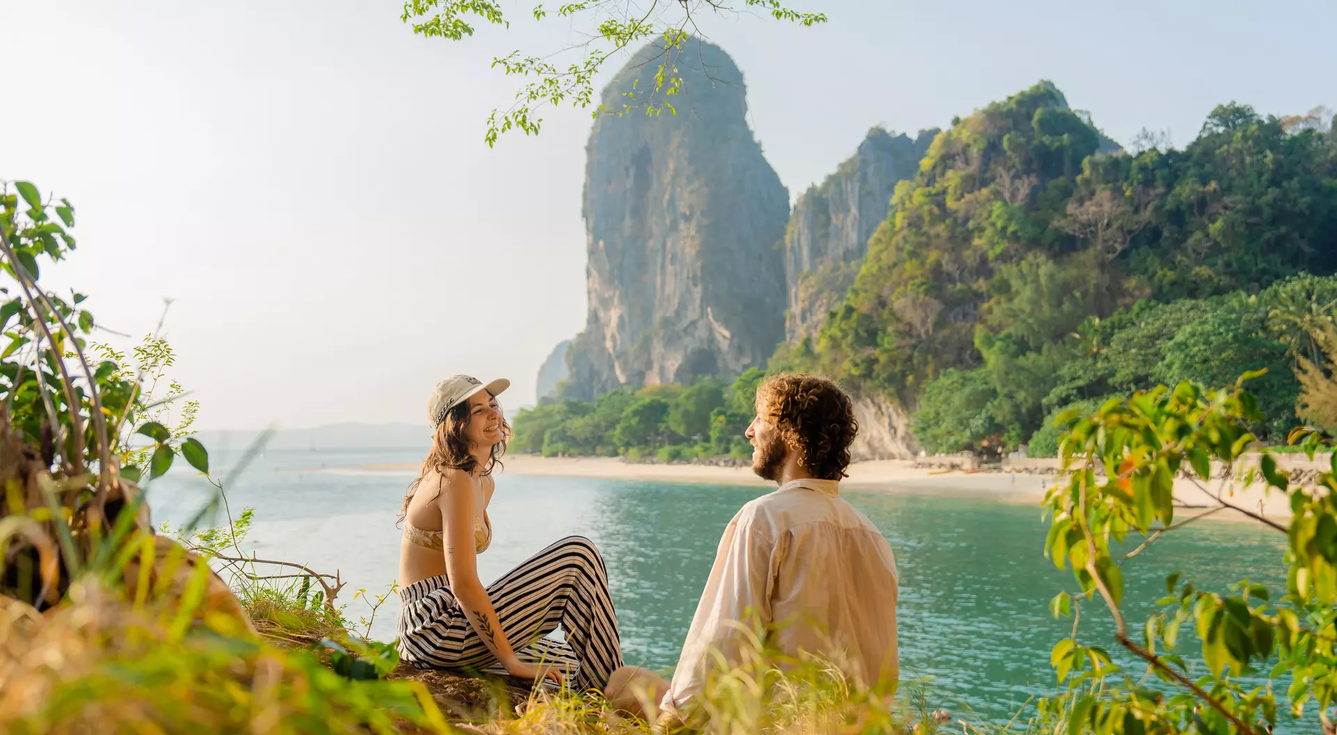A smiling couple in the foreground overlooking Raleigh Beach, Thailand.