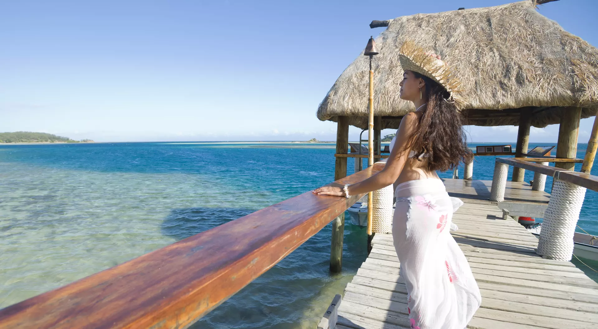 Fiji Woman standing on a Jetty on tropical island with grass hut
