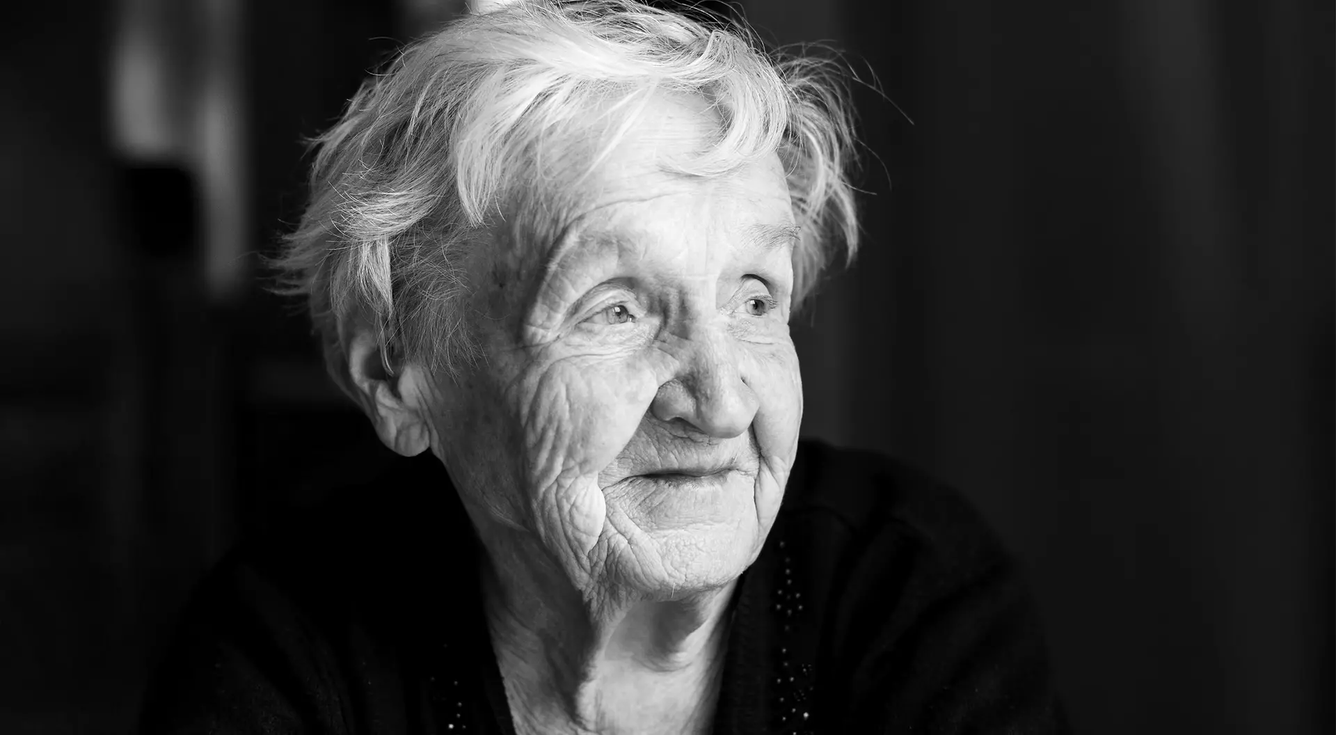 An old woman in black and white looking to the right of the frame.