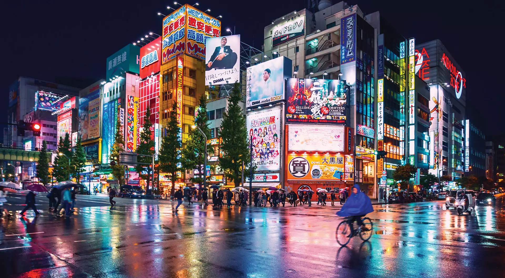 Pedestrians walking and biking in front of a brightly lit and colourful intersection in Tokyo
