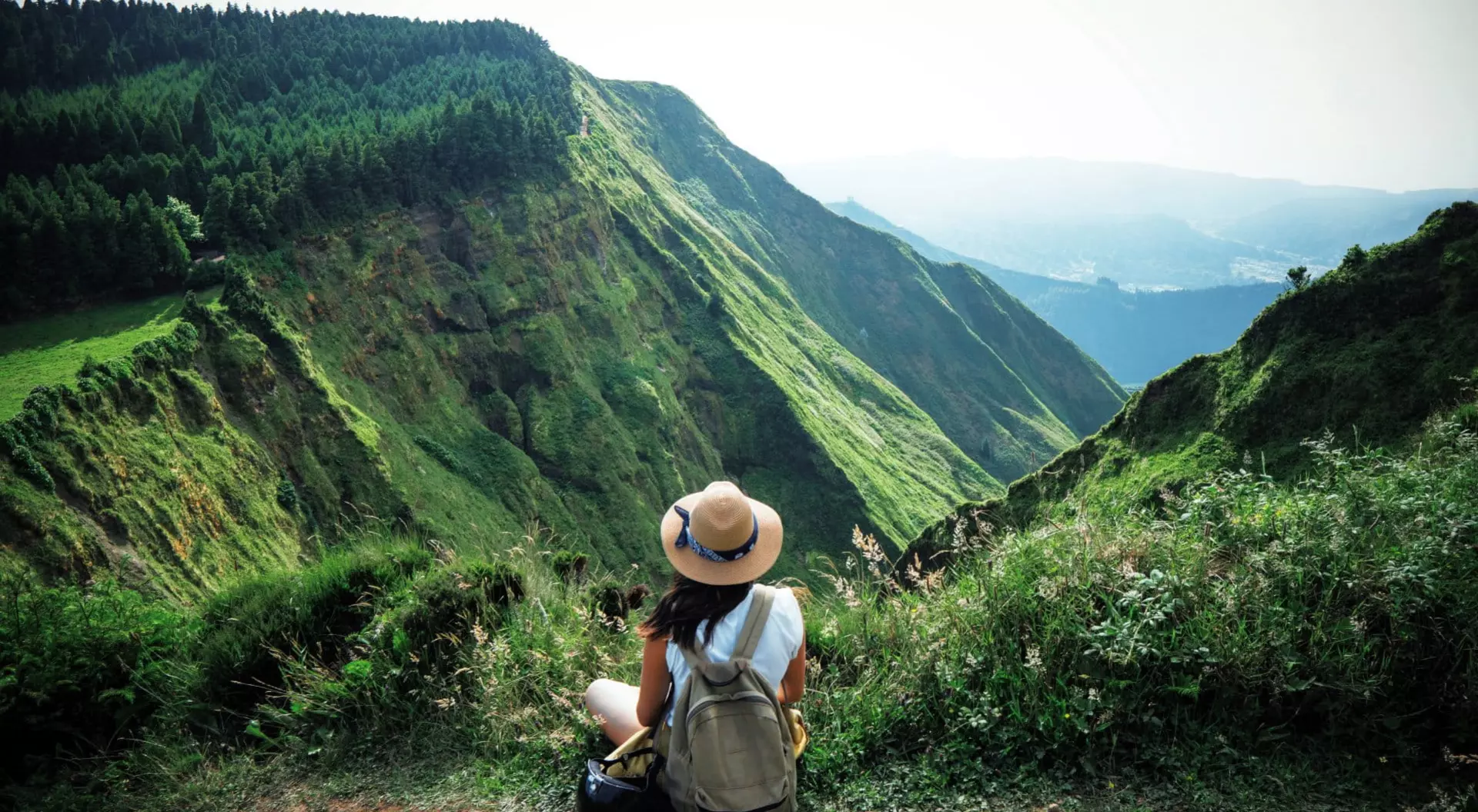 woman sitting on edge of hillside overlooking green mountains